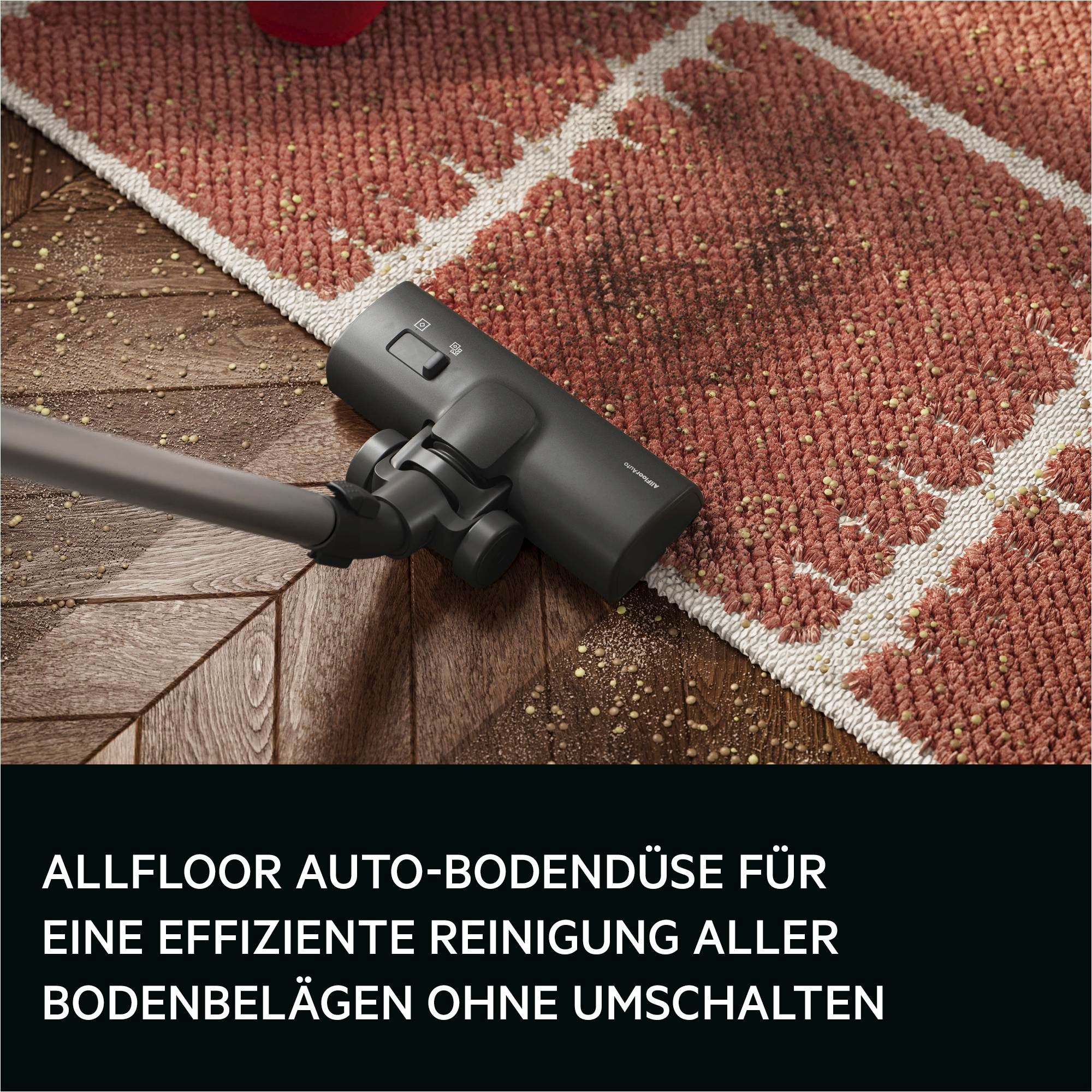 Ein dunkler Staubsaugerkopf auf einem Holzboden und einem Teppich mit Schmutz.