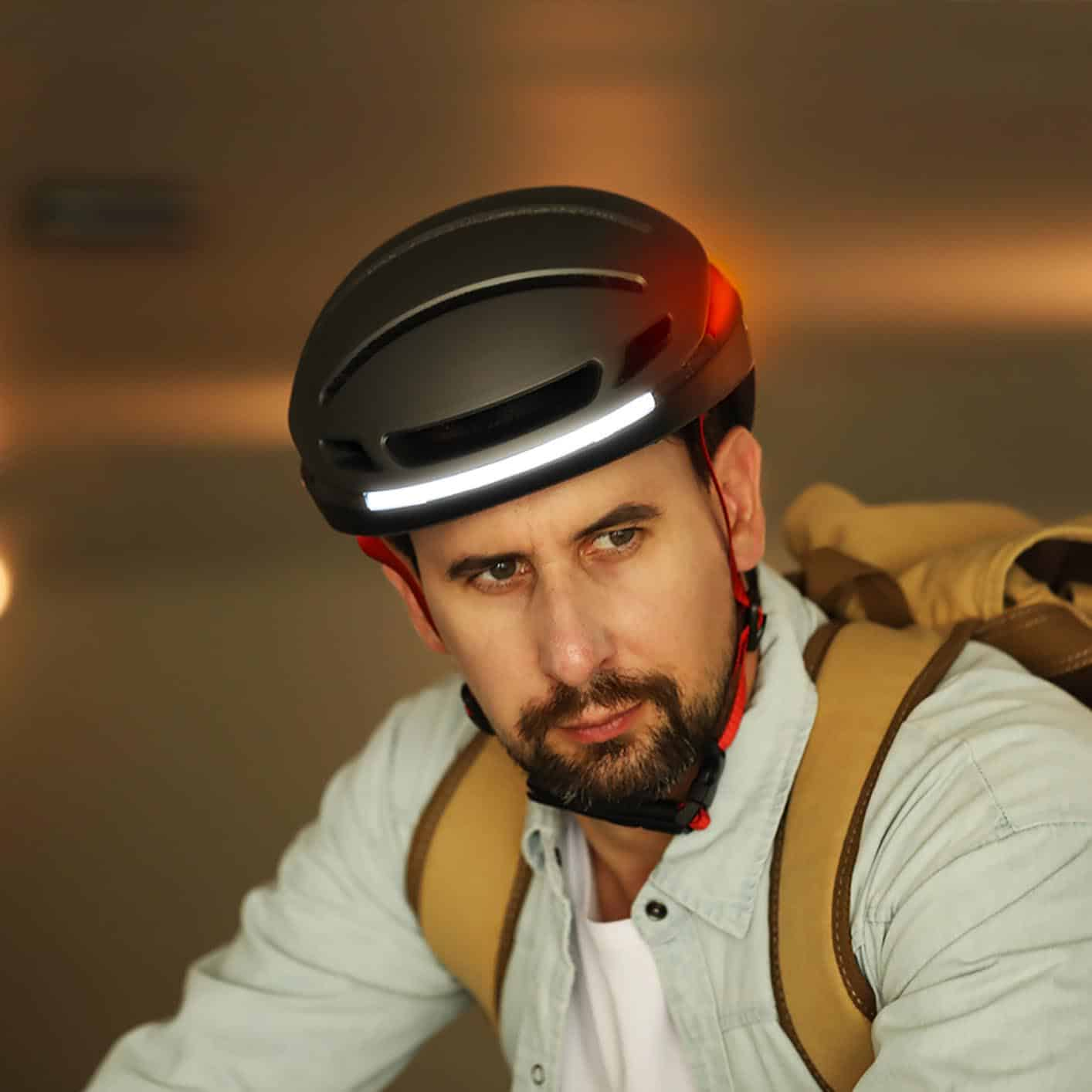 Mann mit schwarzem Fahrradhelm mit roten und weißen Lichtern, trägt Rucksack.