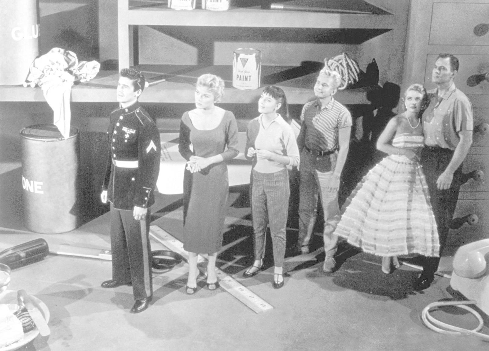 Sechs Personen stehen vor Regalen mit Farbe und Kleber. Ein Mann in Uniform.