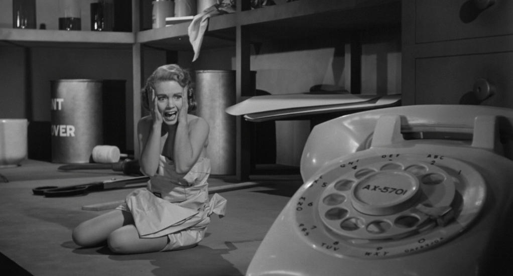 Eine schreiende Frau kniet vor einem Telefon in einem unordentlichen Raum.