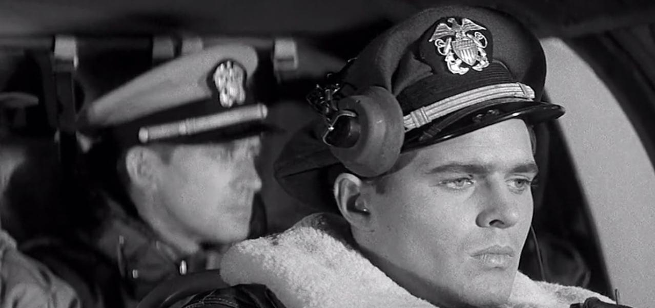 Zwei Männer in Uniformen und Mützen sitzen im Cockpit eines Flugzeugs.