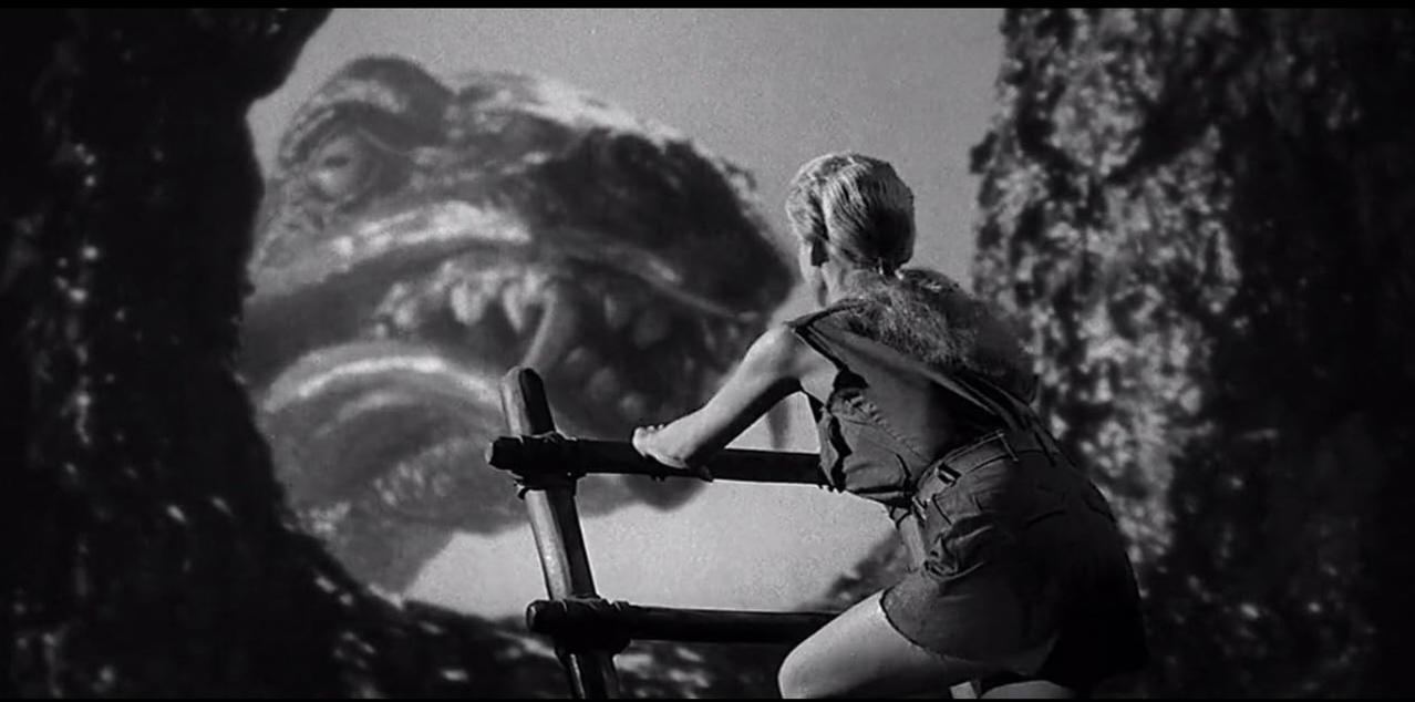 Eine Frau blickt auf ein riesiges Monster-Maul vor einem Felsen.
