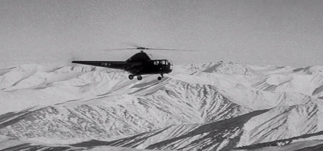 Ein Hubschrauber fliegt über schneebedeckte Berge.