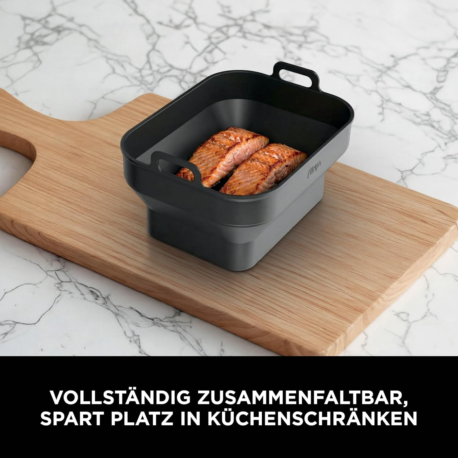 Zwei gebratene Lachsfilets in einem schwarzen, faltbaren Behälter auf einem Holzbrett.