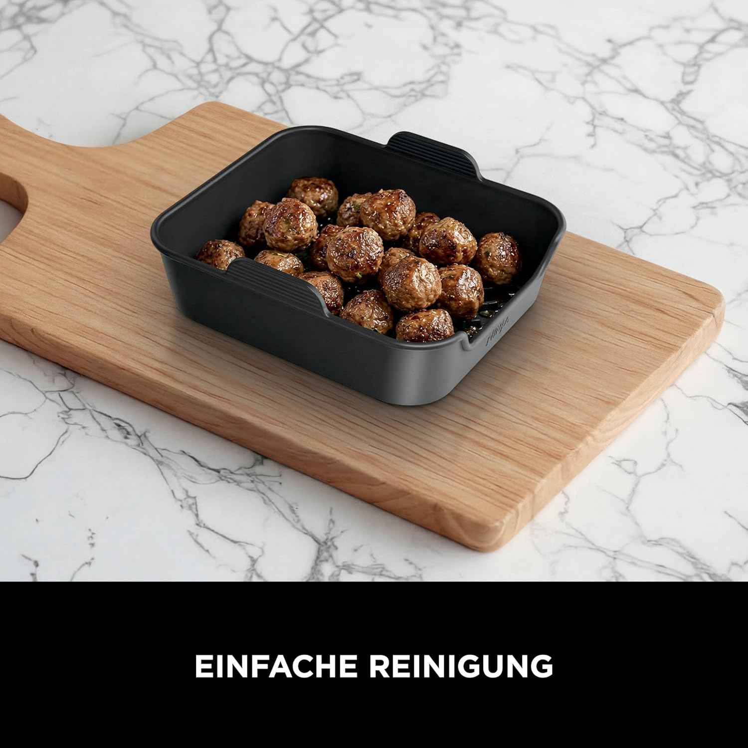 Ein schwarzer Behälter mit vielen braunen Fleischbällchen auf einem Holzbrett.