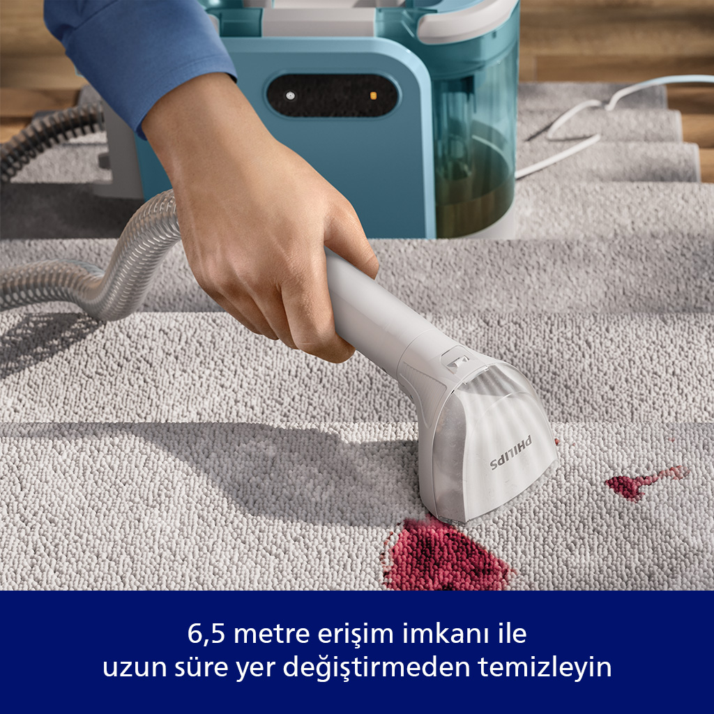 Bir el, gri halıdaki kırmızı lekeleri çıkarmak için beyaz bir temizlik cihazı kullanıyor.