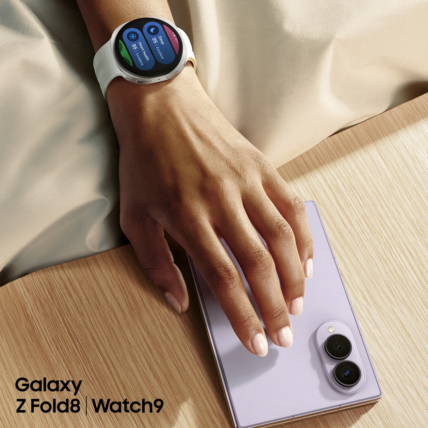 Eine Person trägt eine weiße Smartwatch am Handgelenk neben einem fliederfarbenen Smartphone.