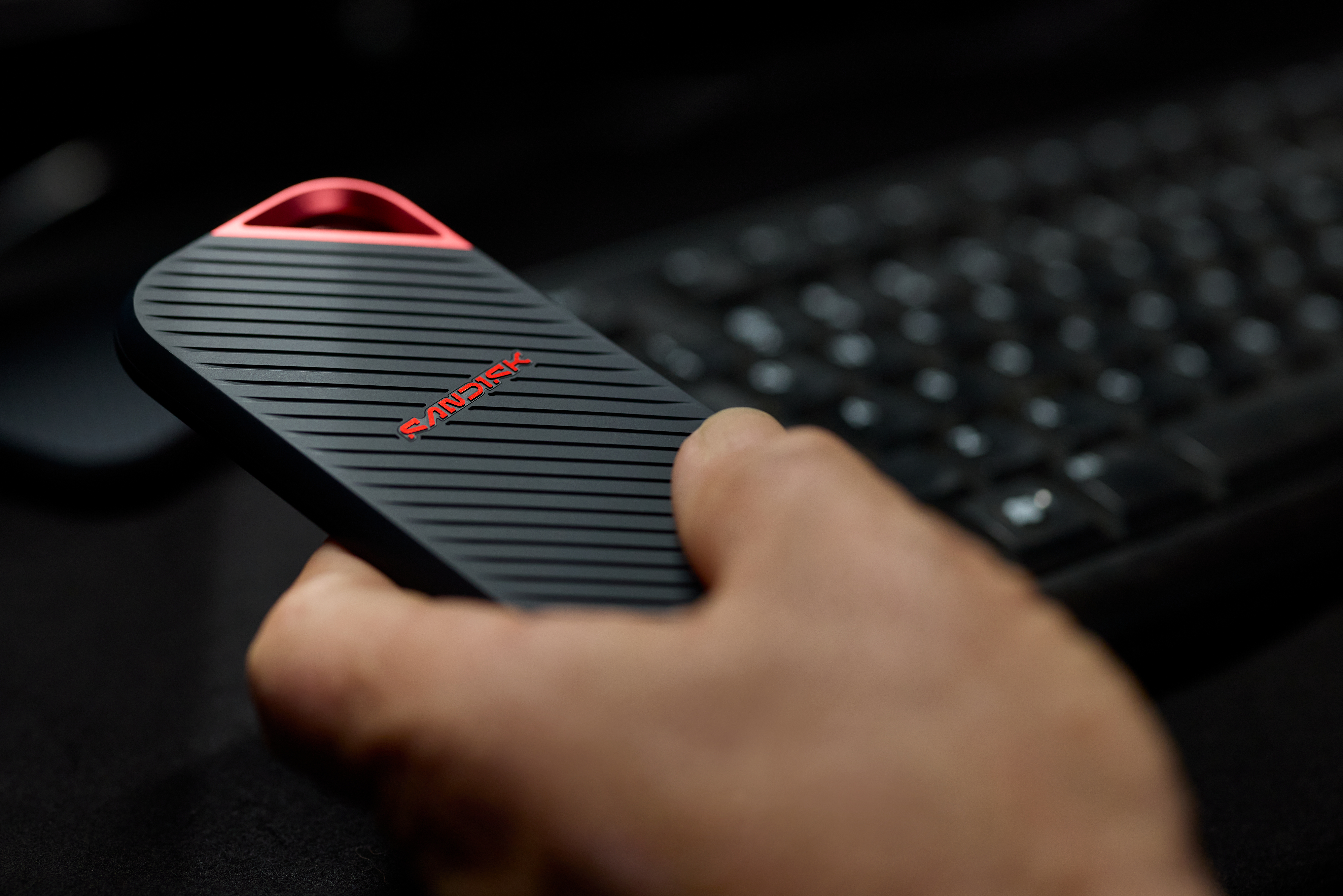Hand hält schwarze SanDisk SSD mit rotem Logo neben Tastatur.