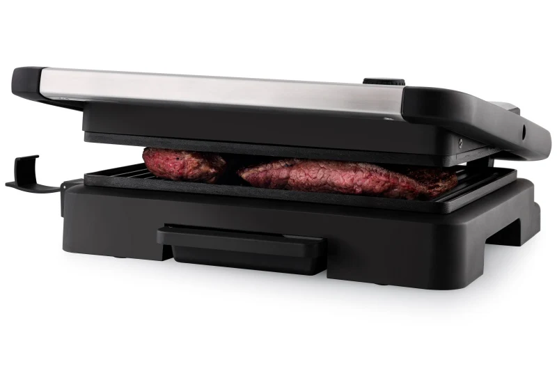 Nyitott kontaktgrill két nyers steakkel a grilllemezen.