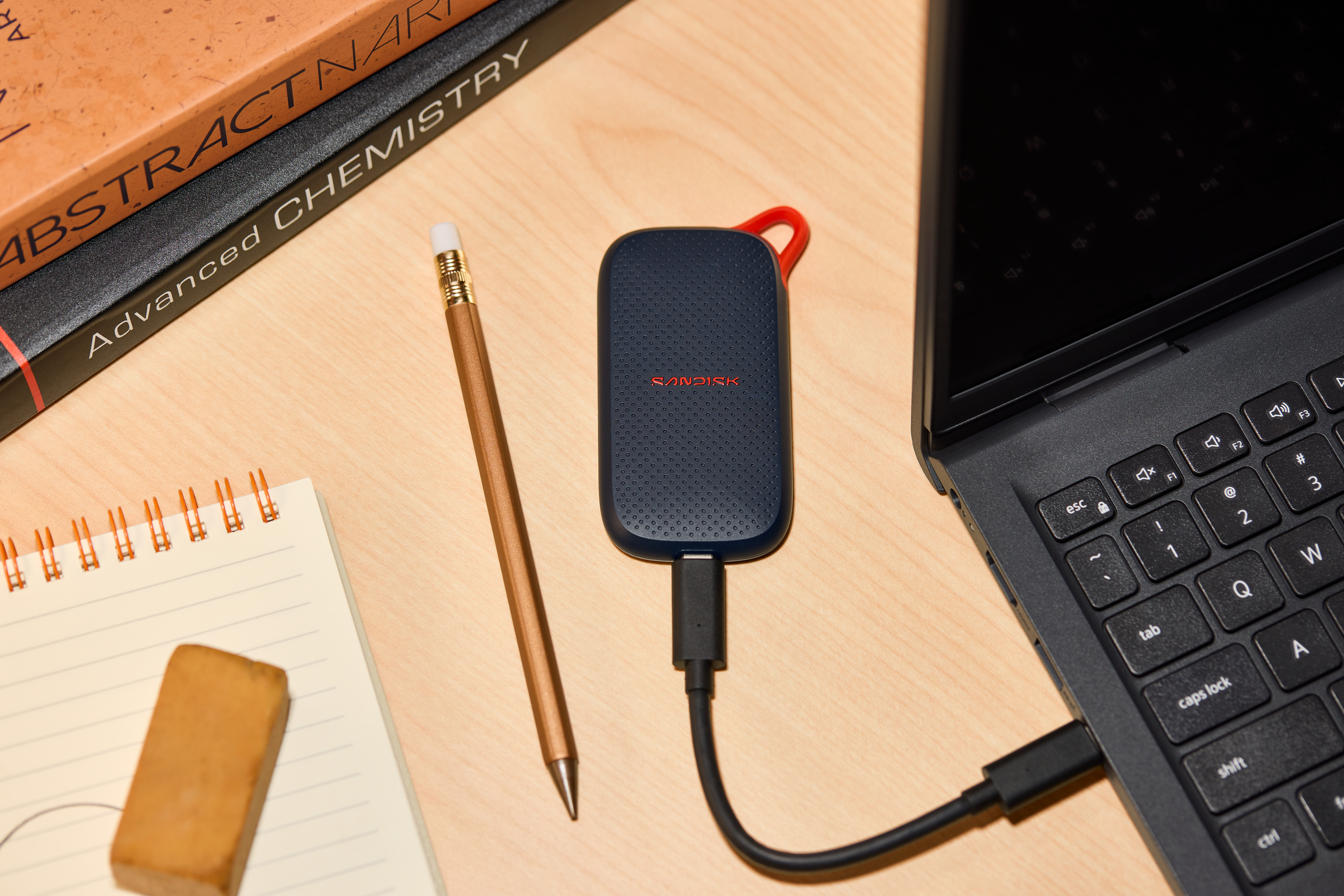 Ein dunkler SanDisk SSD auf einem Holztisch, verbunden mit einem Laptop.