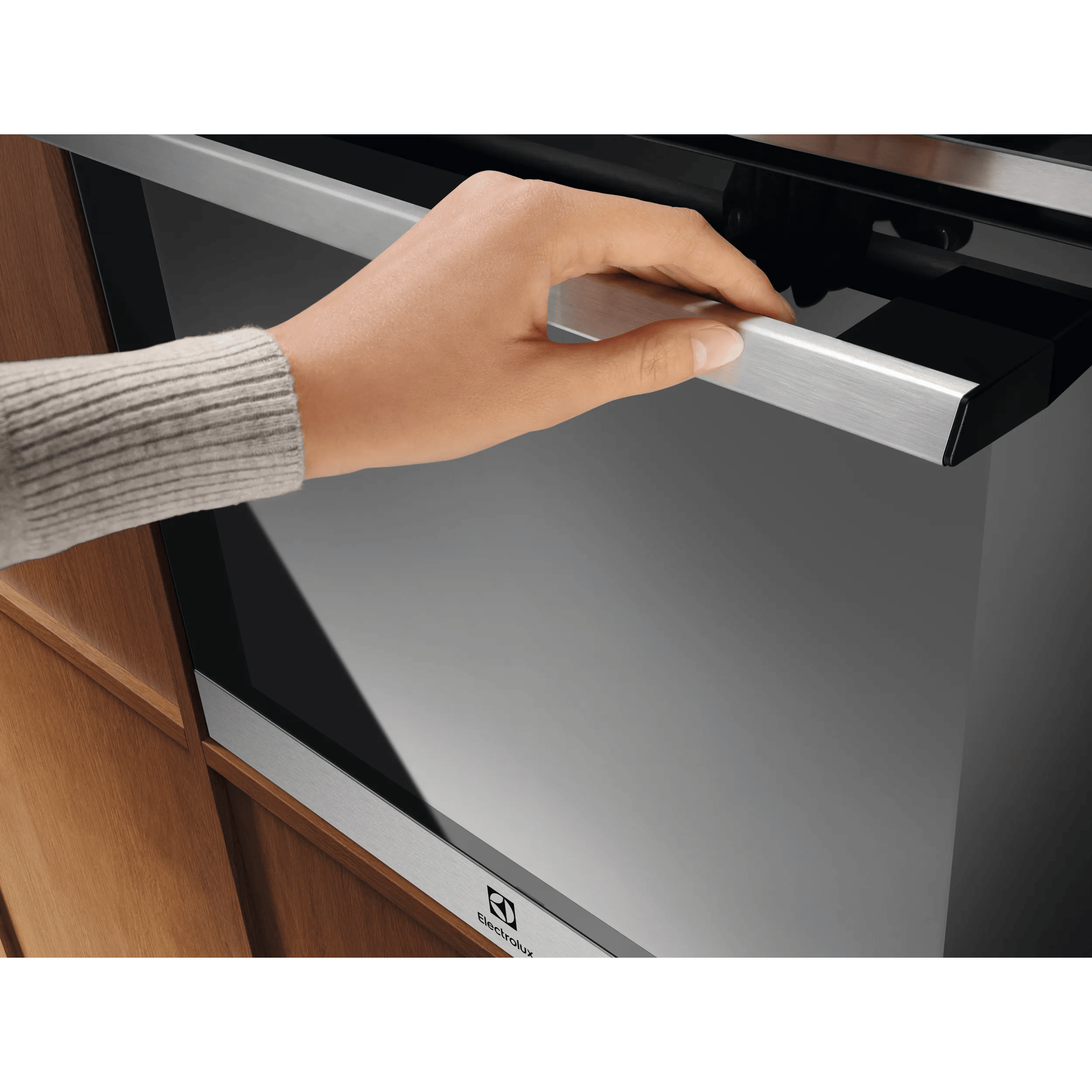 Ręka otwiera nowoczesne drzwi piekarnika Electrolux z srebrną klamką.