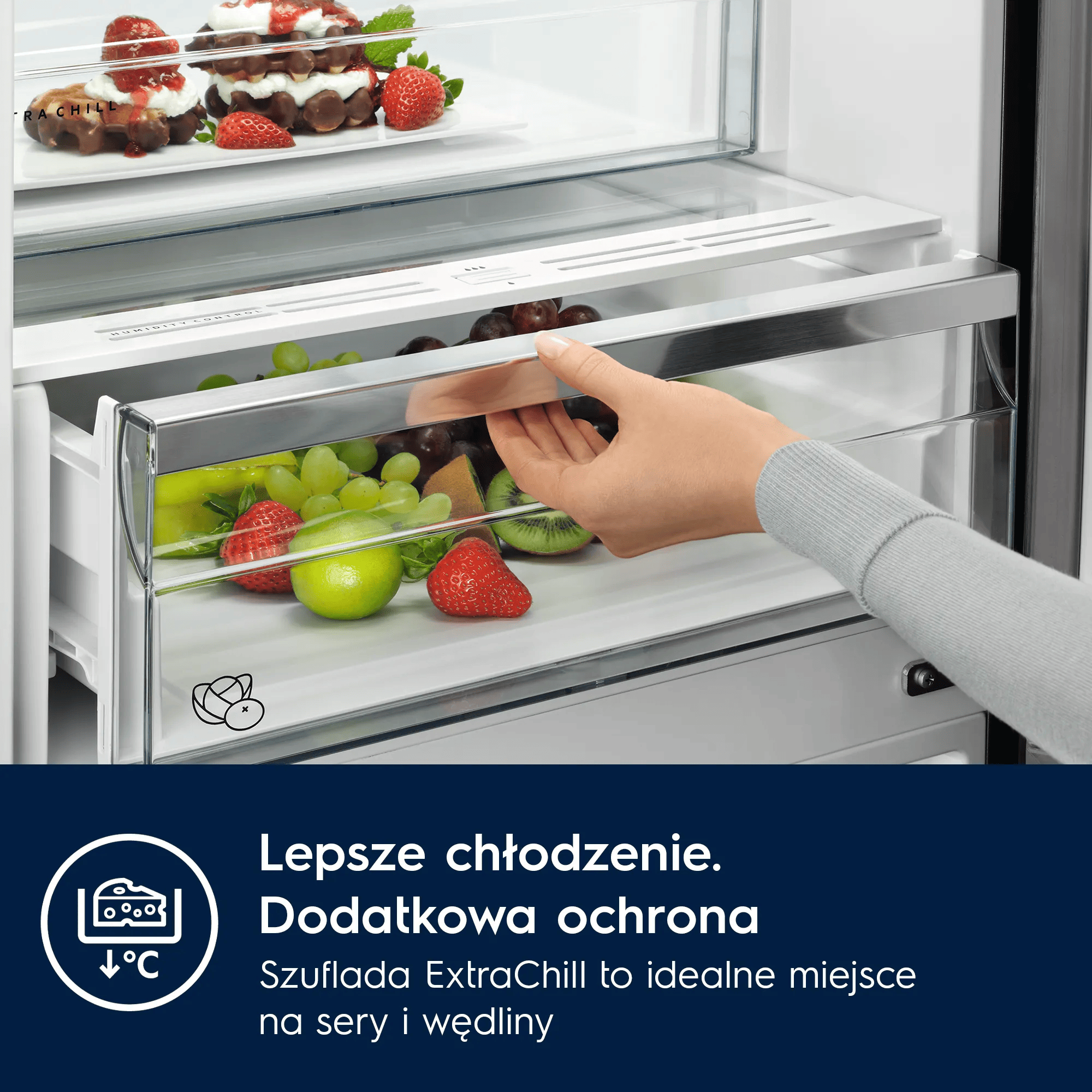 Ręka otwiera szufladę lodówki z owocami i truskawką na pierwszym planie.