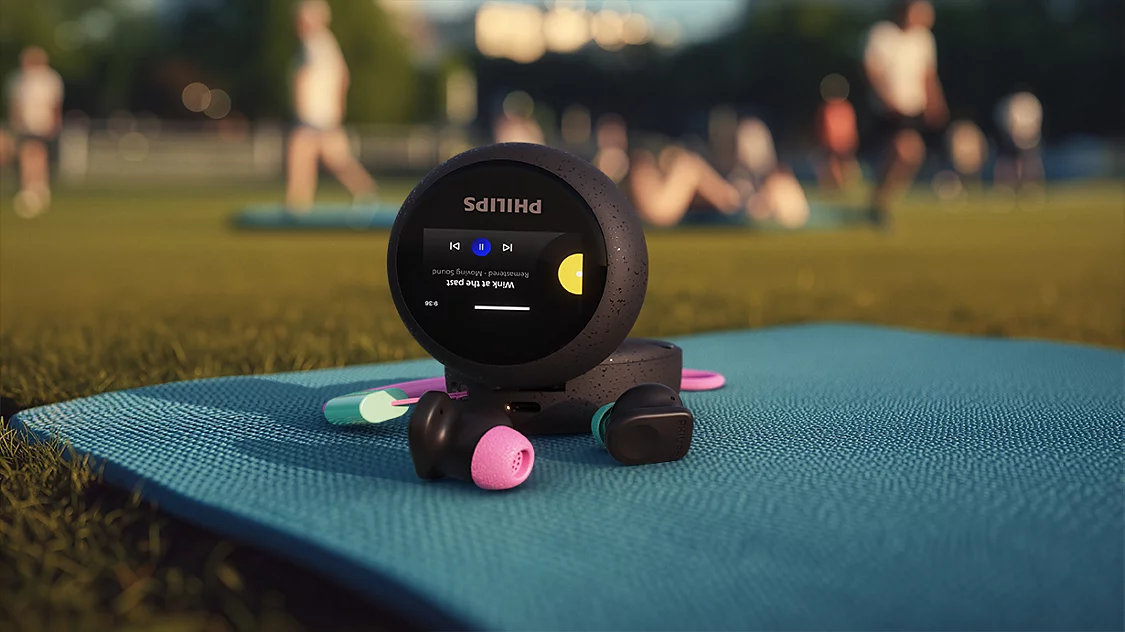 Philips Kopfhörer auf Matte im Freien, mit unscharfen Personen im Hintergrund.