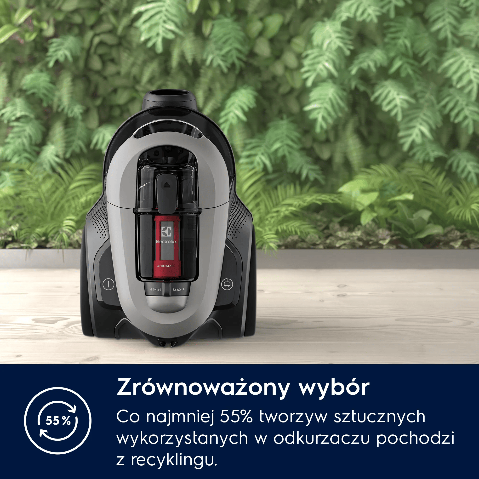 Szary i czarny odkurzacz na drewnianej podłodze przed zielonymi roślinami.