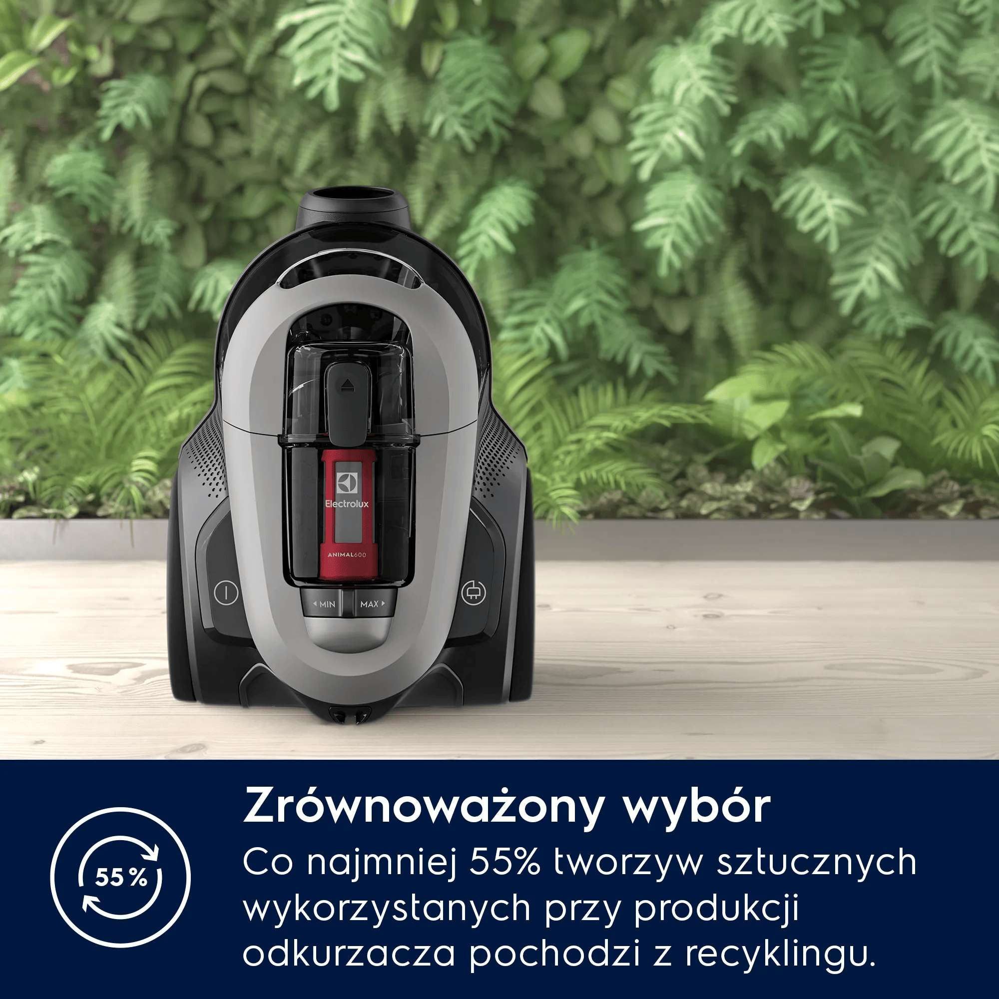 Czarny i szary odkurzacz stoi na drewnianym stole przed zielonymi roślinami.