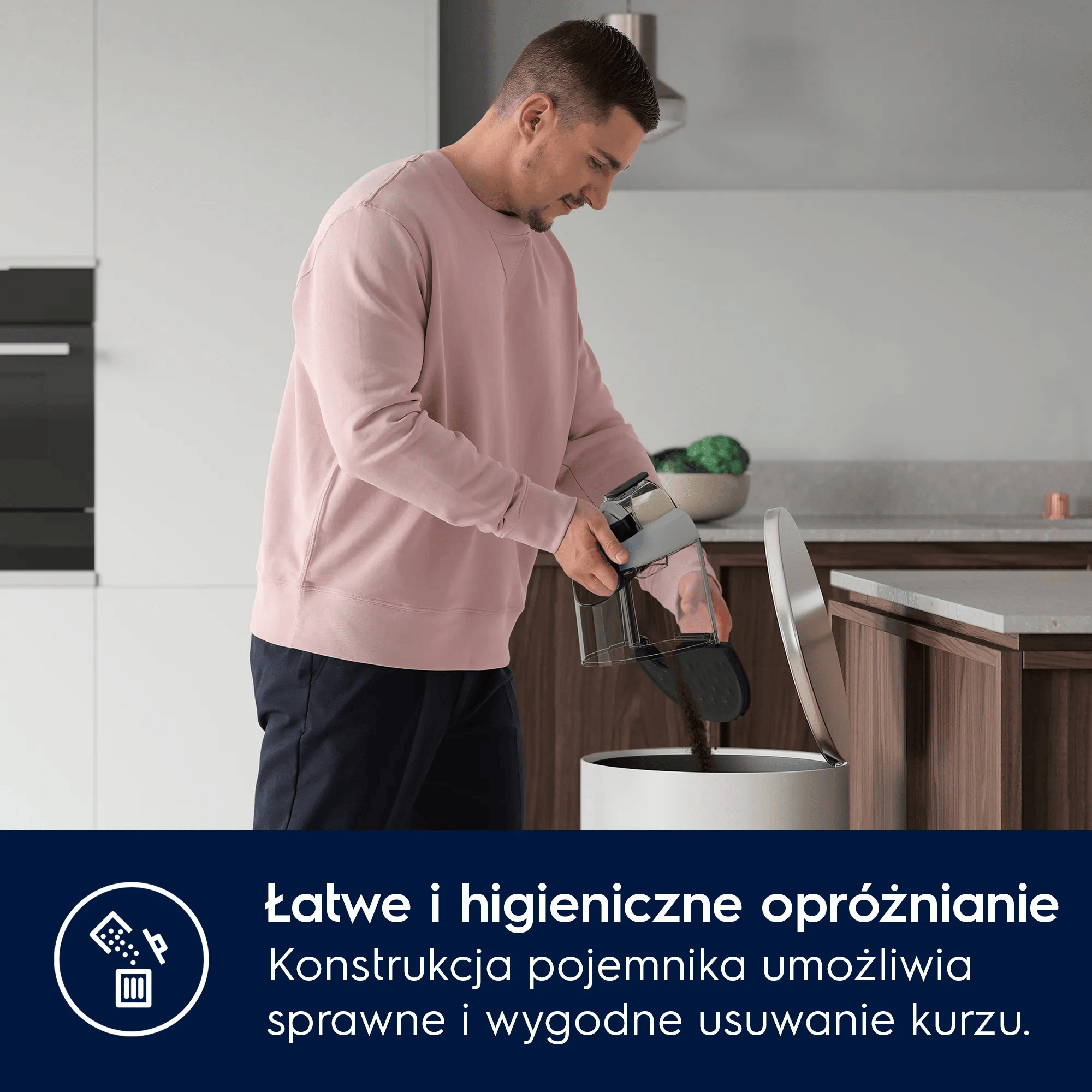 Mężczyzna opróżnia pojemnik odkurzacza do kosza w kuchni.