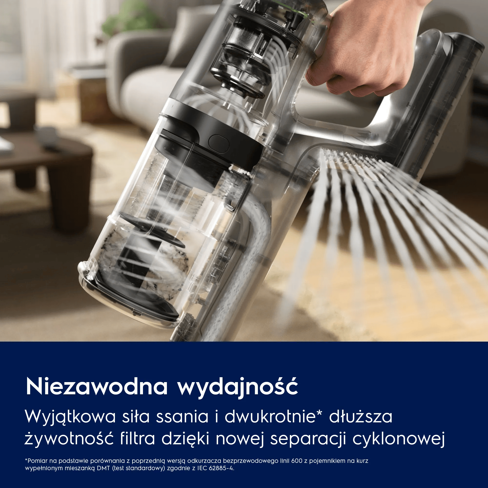 Dłoń trzyma przezroczystą rączkę odkurzacza, unosząc pył.