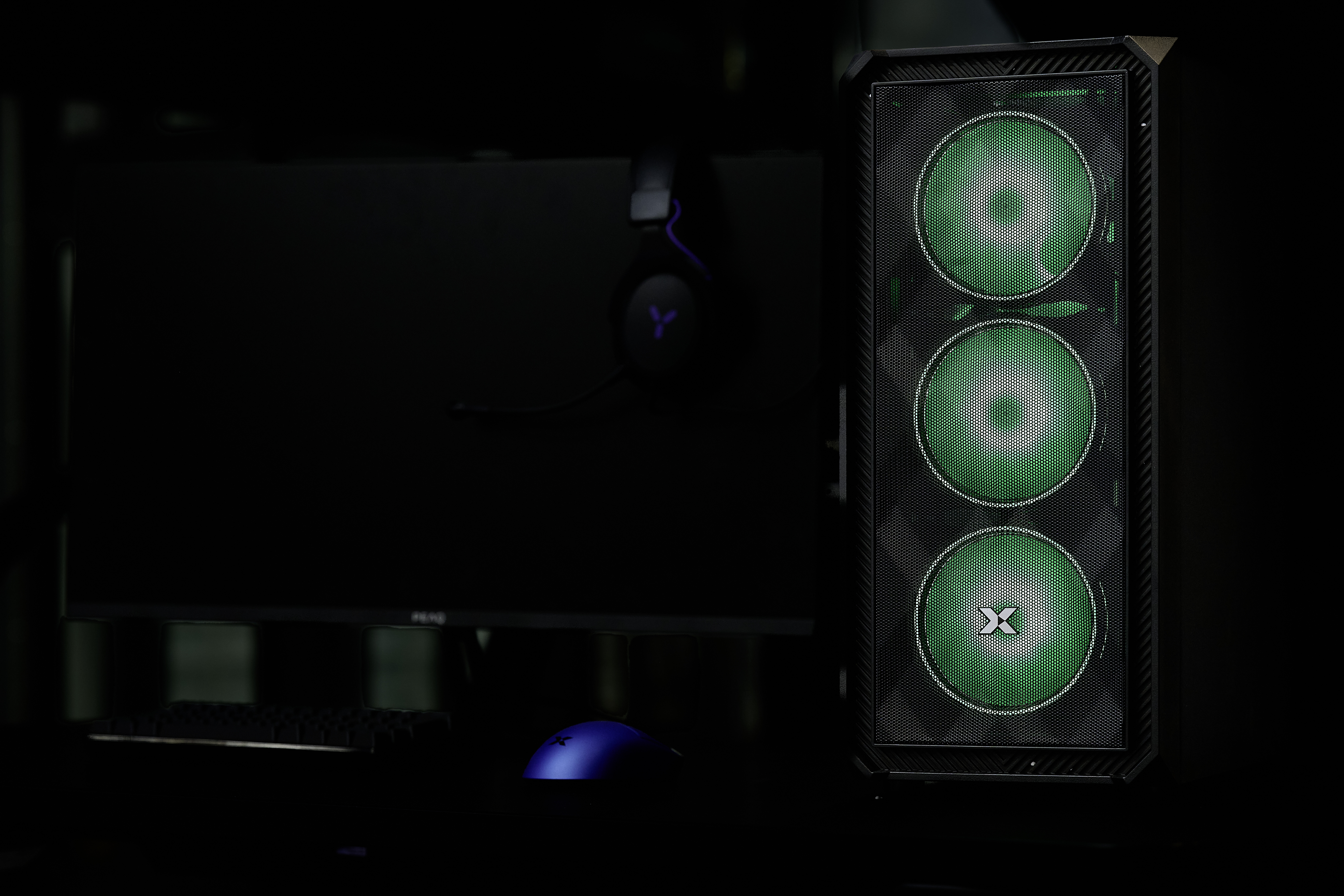 Ein PC-Gehäuse mit grünen Lüftern, daneben ein dunkler Monitor mit Kopfhörern.