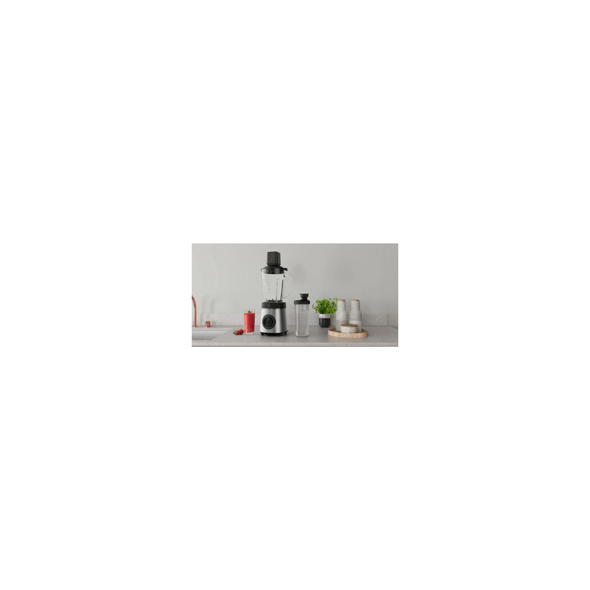 Srebrny blender z szklanym dzbankiem stoi na blacie kuchennym obok szklanki czerwonego soku.