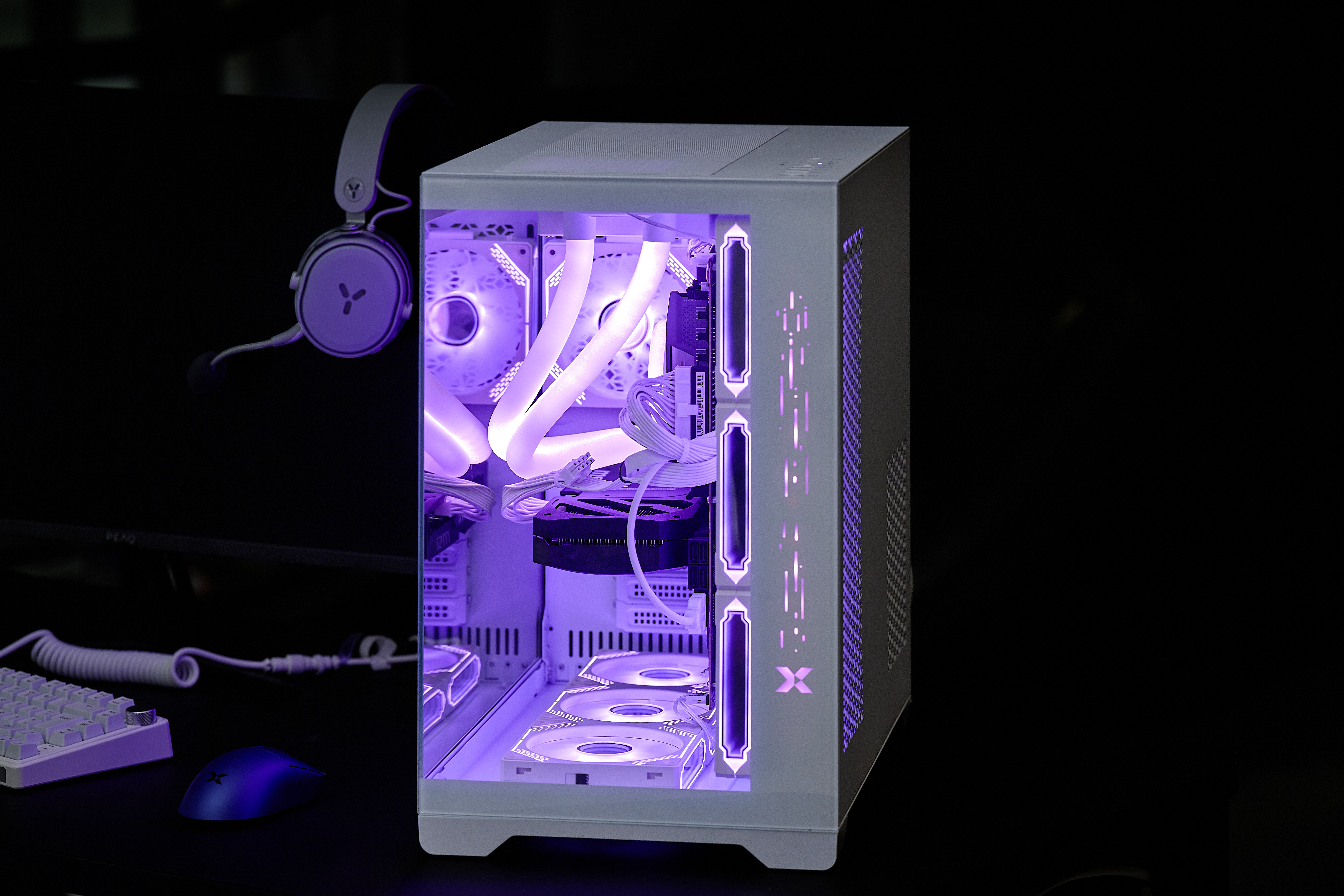 Ein weißer Gaming-PC mit violetter Beleuchtung, Kopfhörer, Tastatur und Maus.
