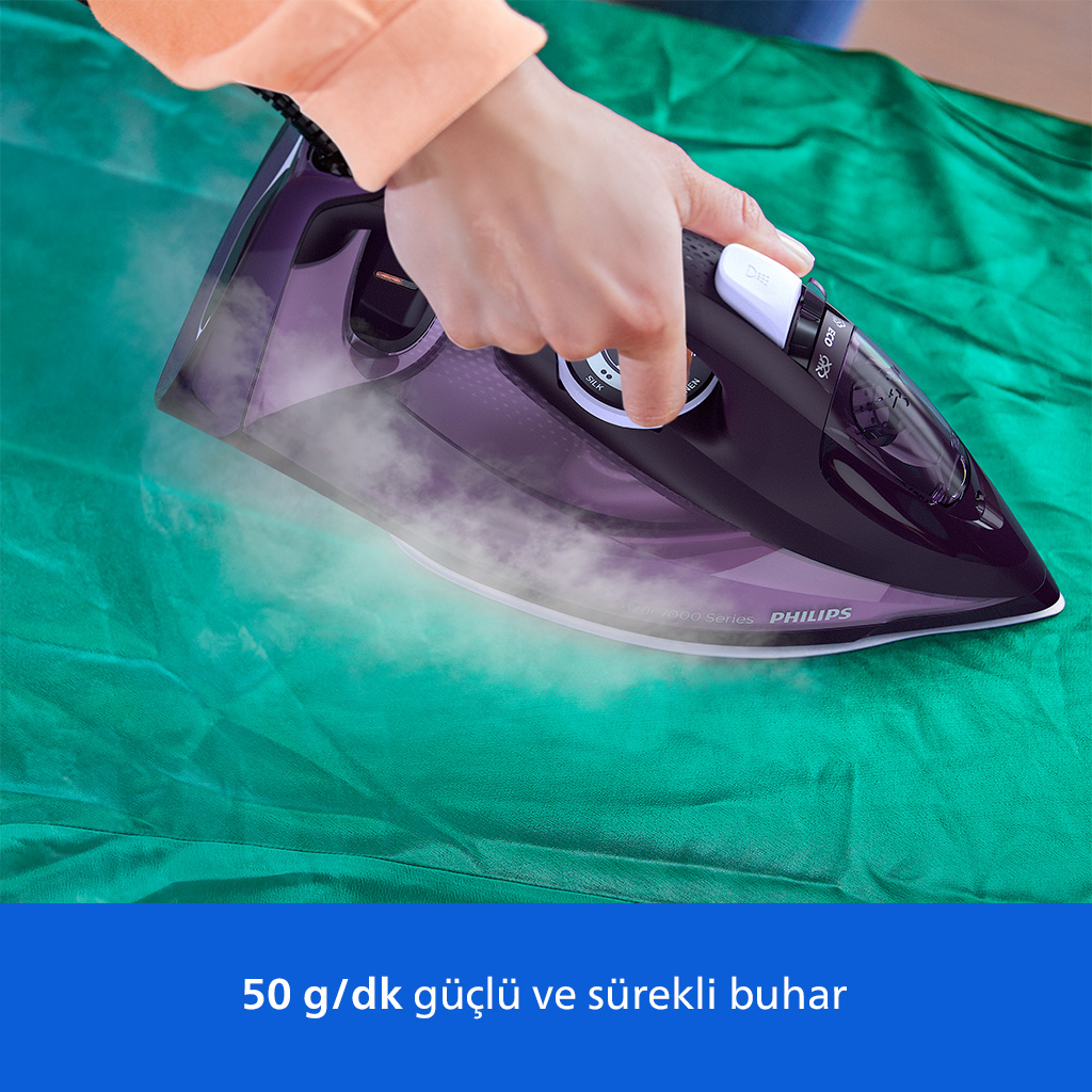 Bir el, mor Philips buharlı ütü ile yeşil kumaşı ütülüyor.