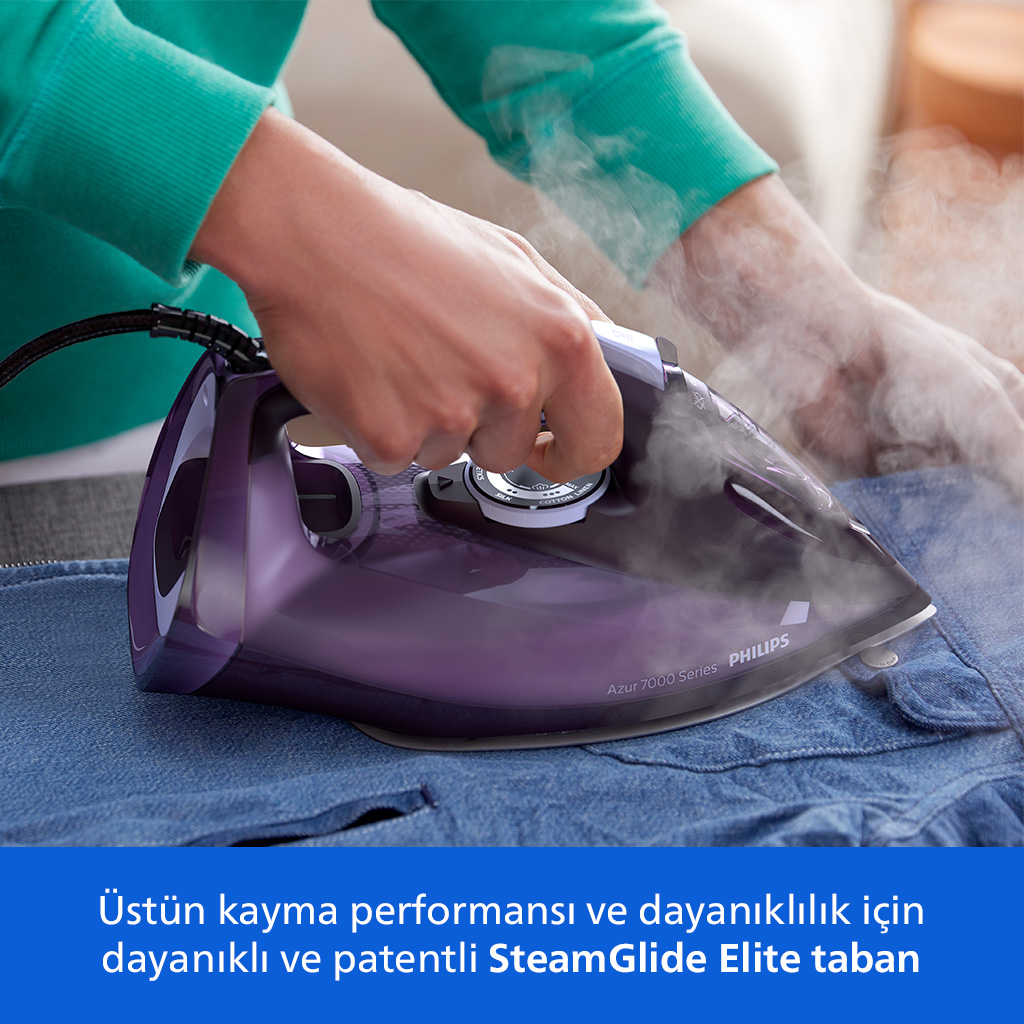 Bir kişi mor buharlı ütü ile mavi kot gömlek ütülüyor, buhar yükseliyor.