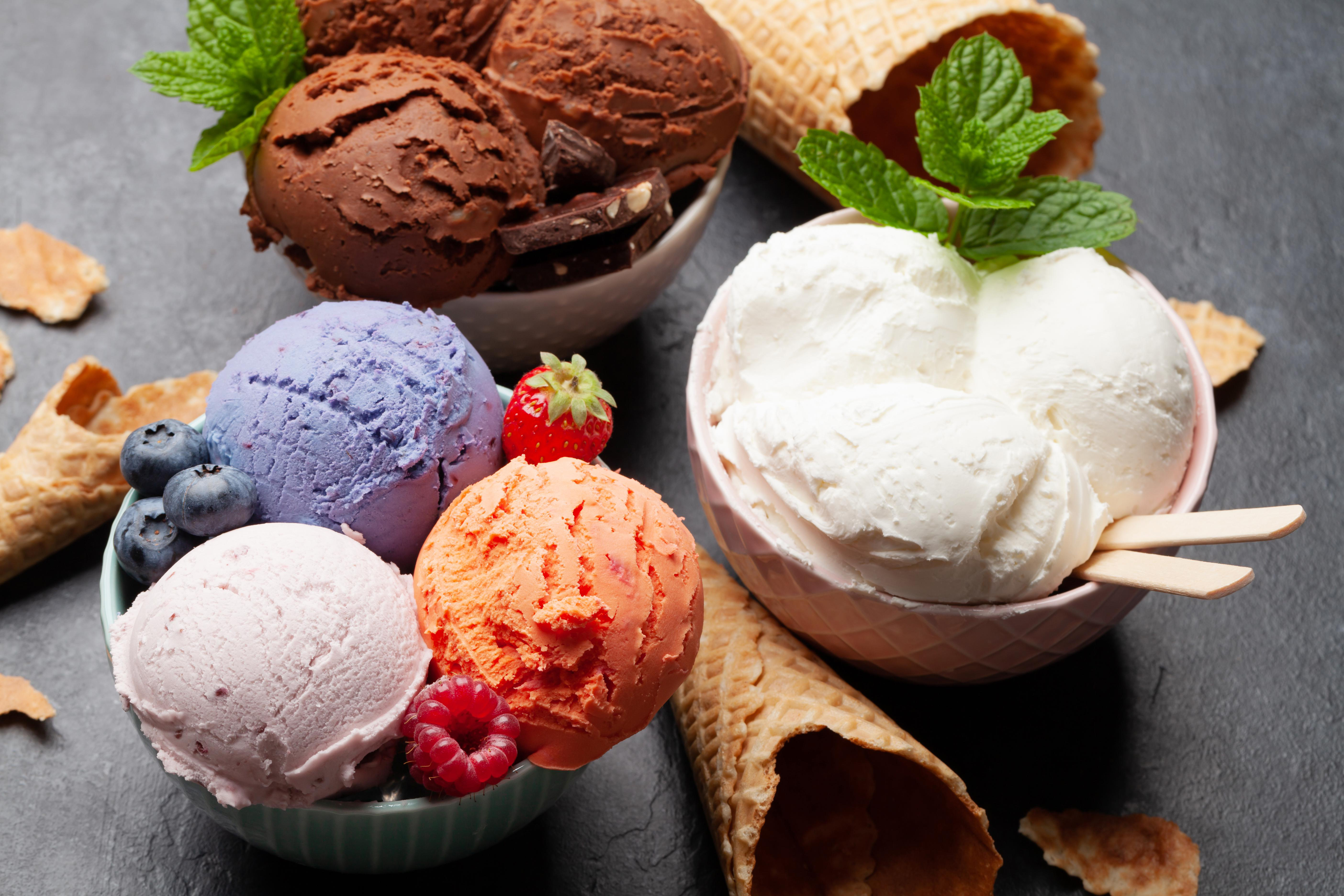 Mehrere Schalen mit Eiscreme in verschiedenen Geschmacksrichtungen: Schokolade, Vanille, Beere und Orange.
