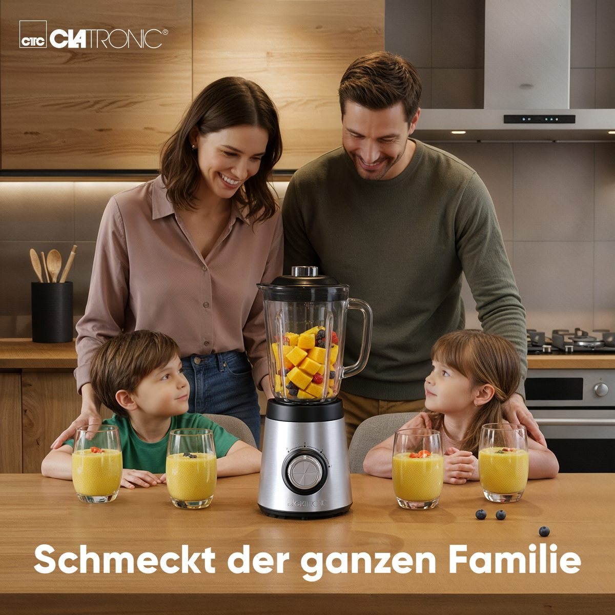 Familie mit Mixer mit Obst und Gläsern Saft am Holztisch.