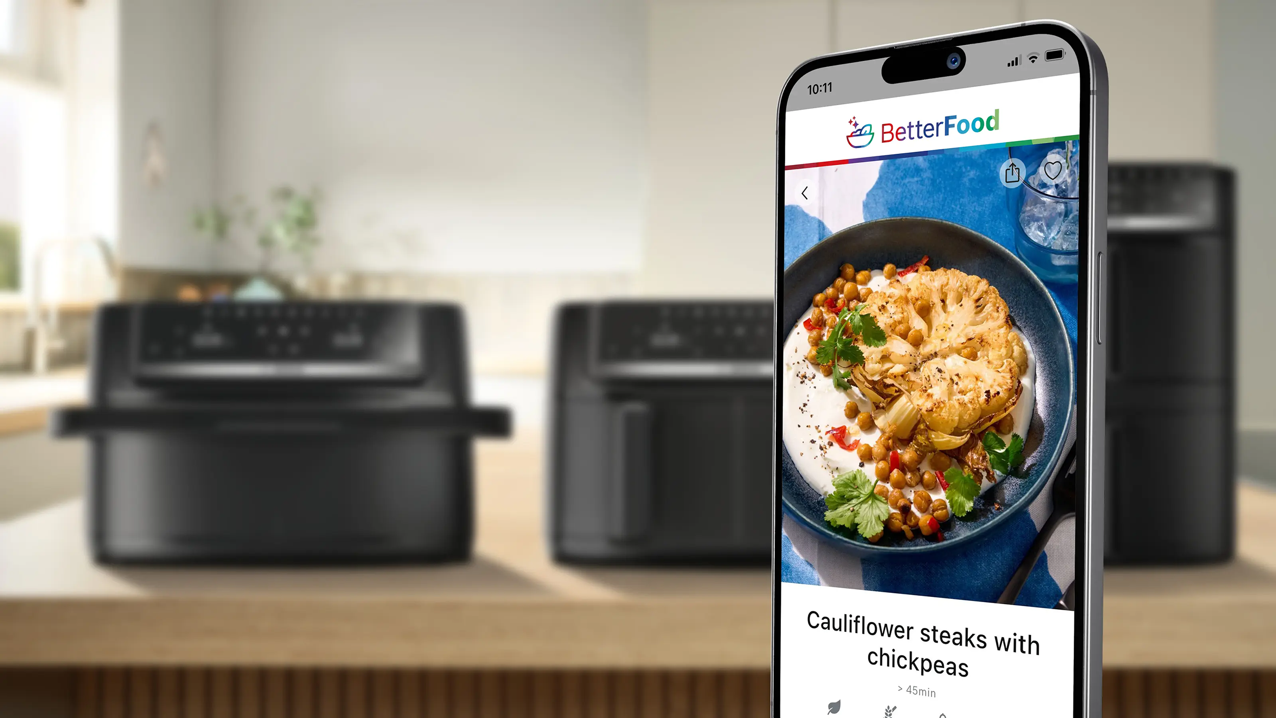 Egy okostelefon receptet mutat karfiolsteakekről csicseriborsóval. Két air fryer a háttérben.