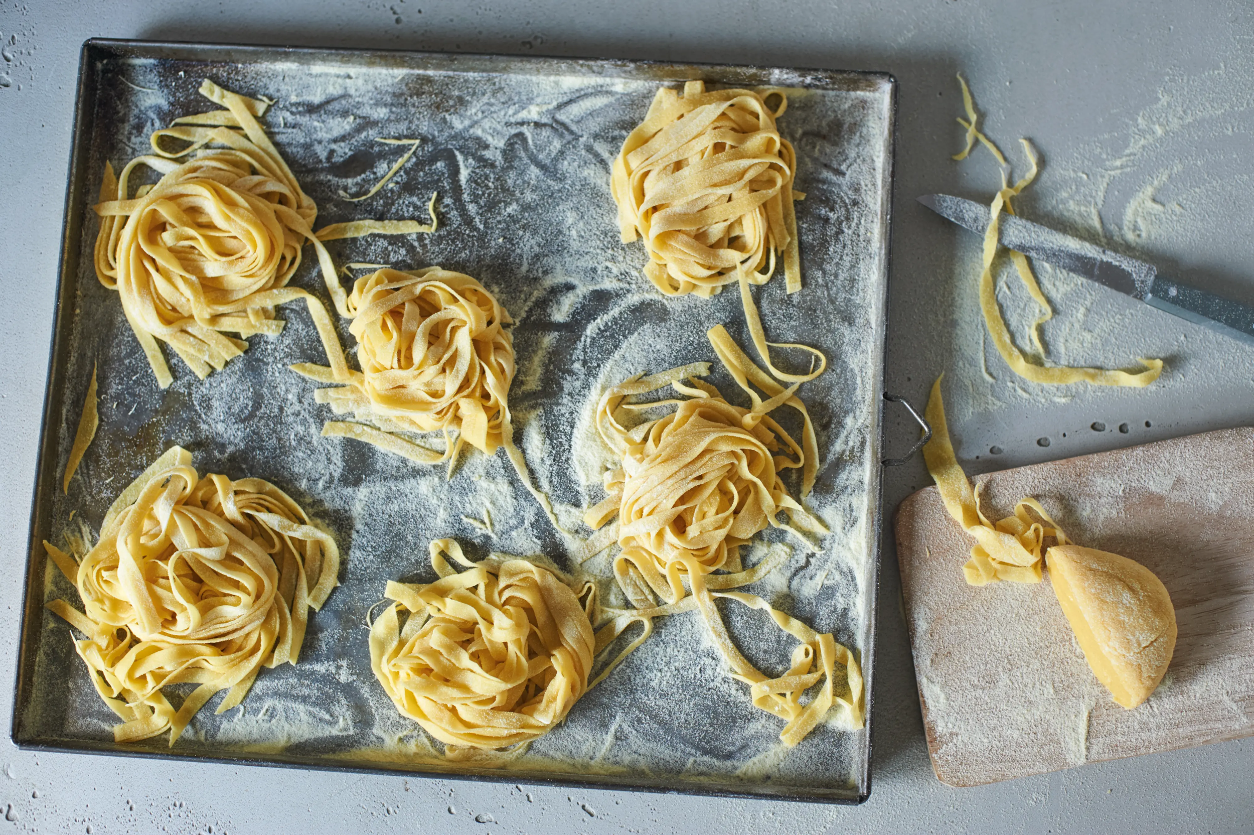 Friss fettuccine tepsiben liszttel, kés és vágódeszka mellett.