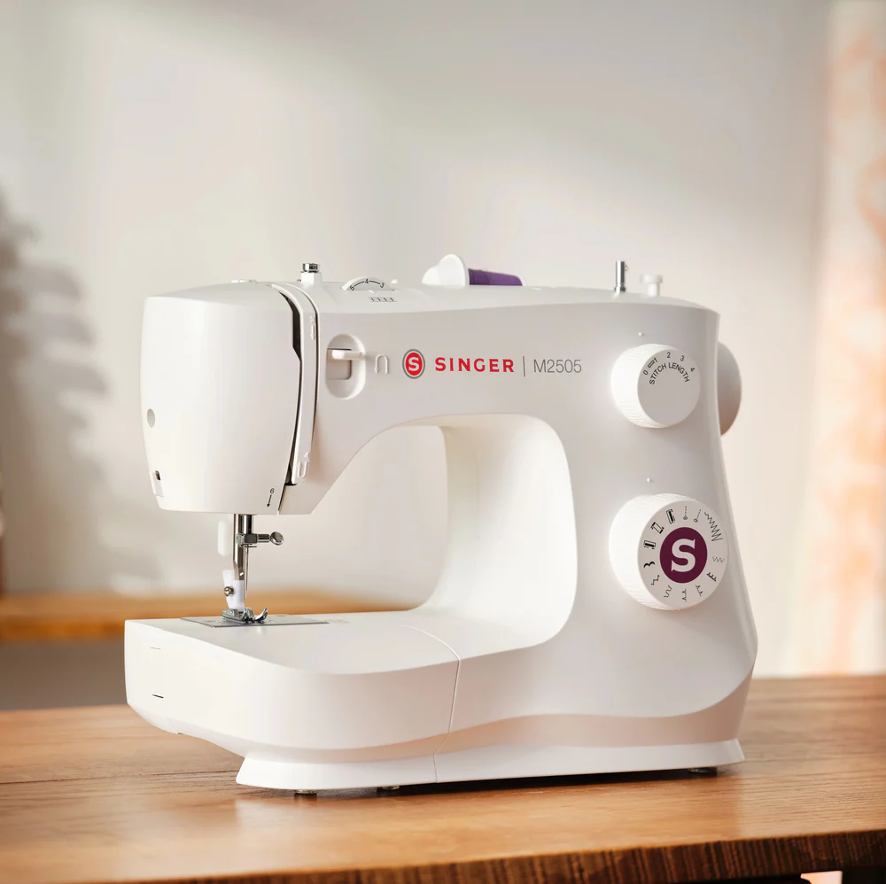 Una máquina de coser Singer M2505 blanca descansa sobre una mesa de madera.