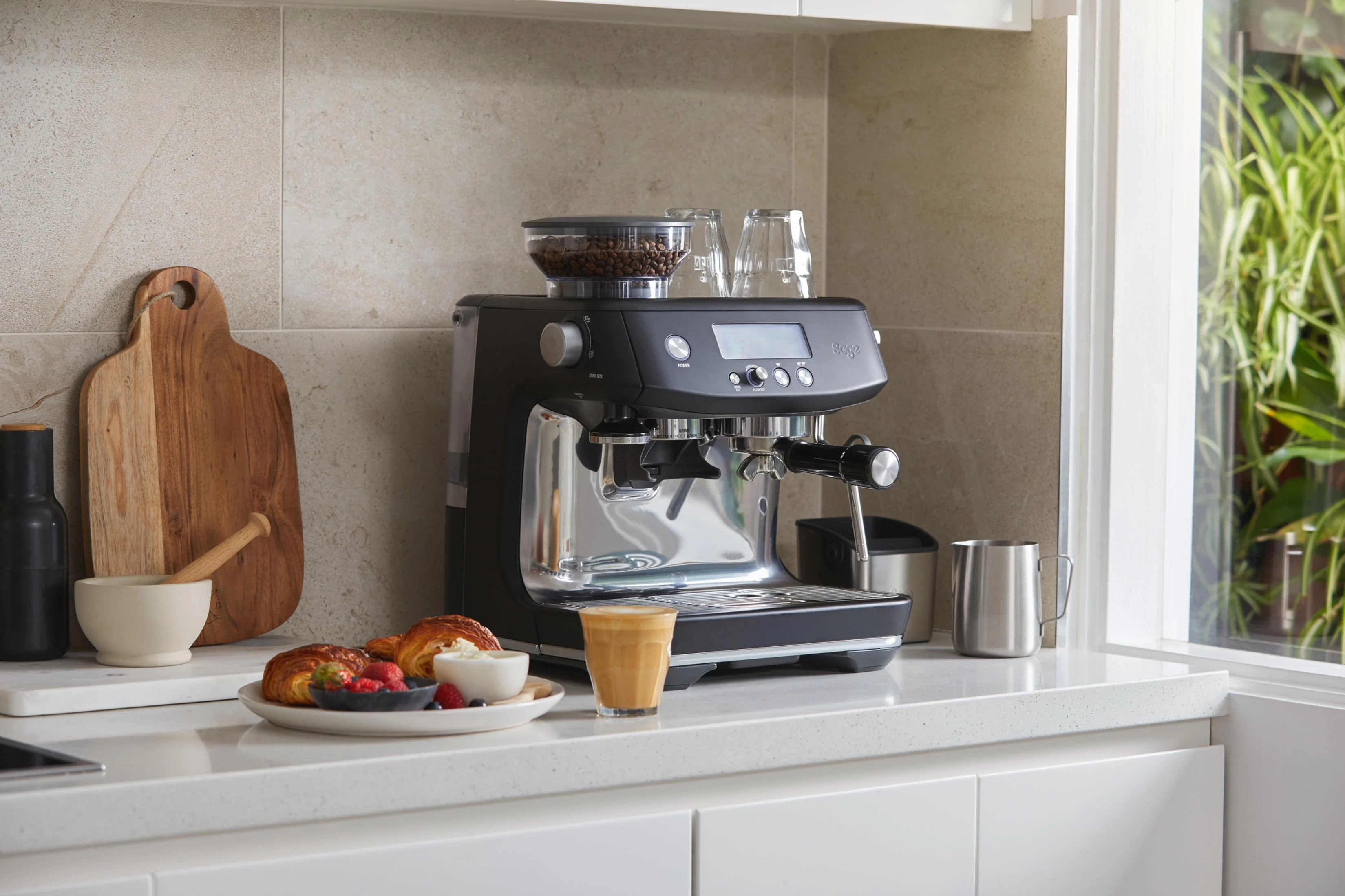 Una máquina de espresso con tolva de granos, pasteles y café al lado.