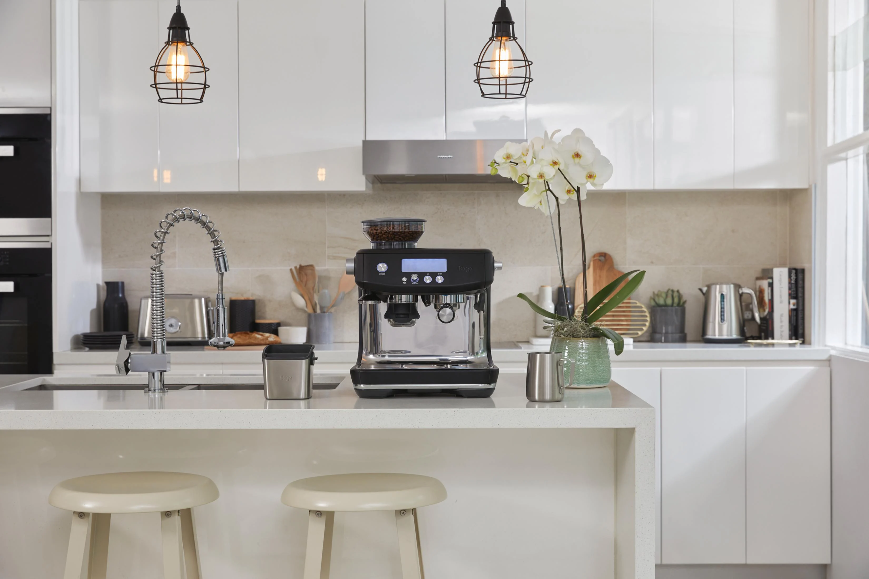 Cocina moderna con cafetera, grifo y orquídeas.