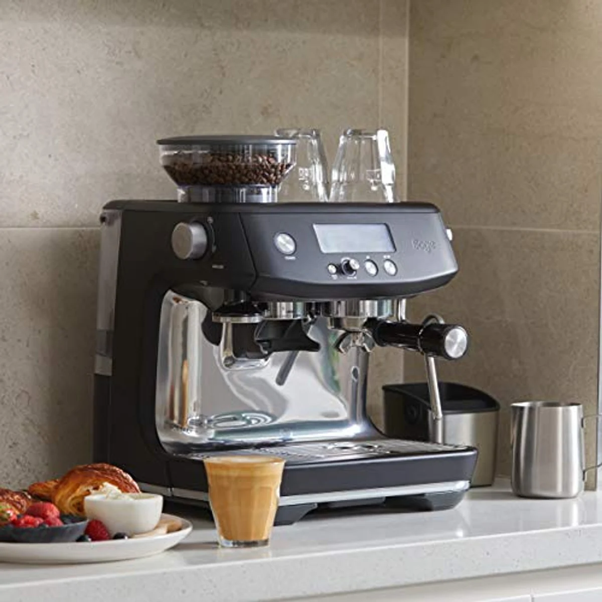 Una máquina de espresso negra con granos de café, vasos, pasteles y café.