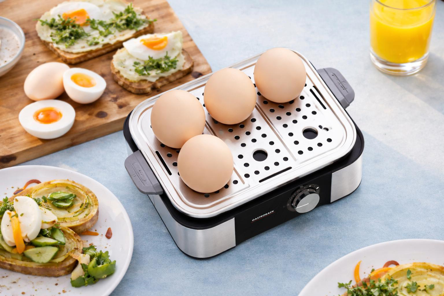 Eierkocher mit vier Eiern, daneben Toast mit Spiegelei und gekochte Eier.