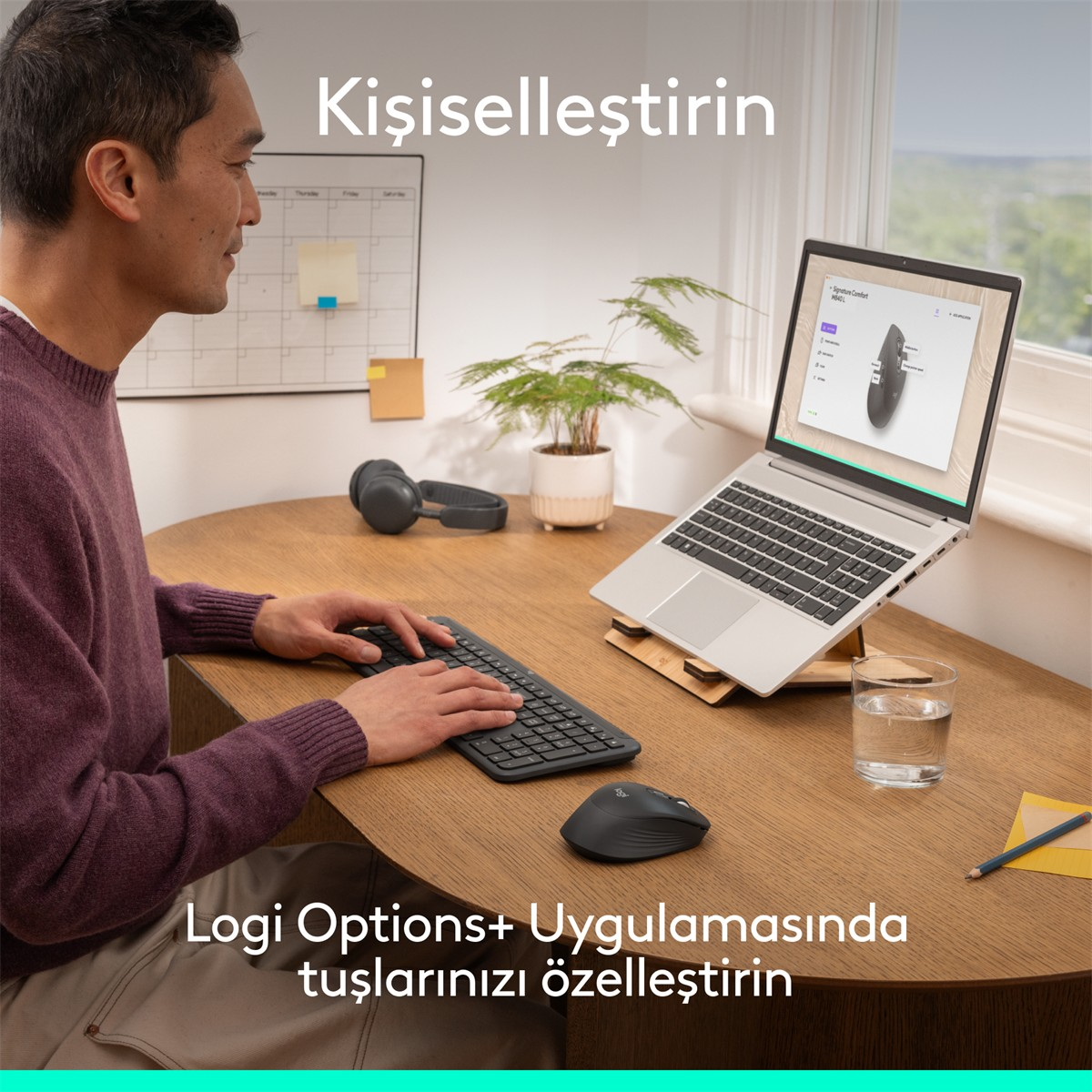 Adam klavyede yazıyor, yanında fare yazılımı gösteren dizüstü bilgisayar, kulaklık ve su bardağı.