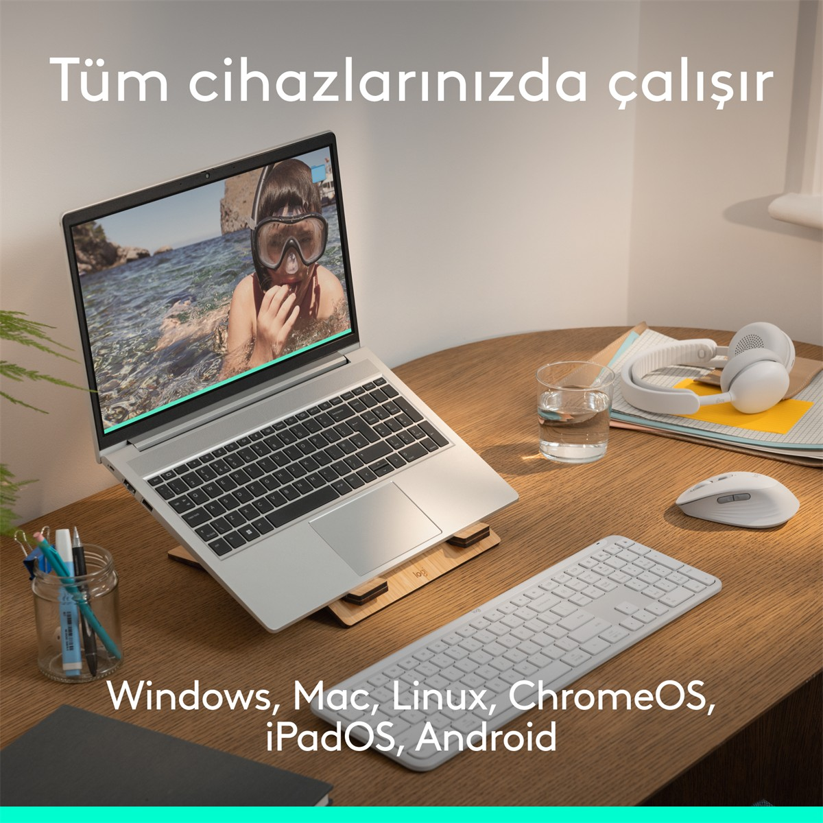 Dalgıç maskeli bir çocuğun göründüğü laptop, klavye, fare, kulaklık ve su bardağı.