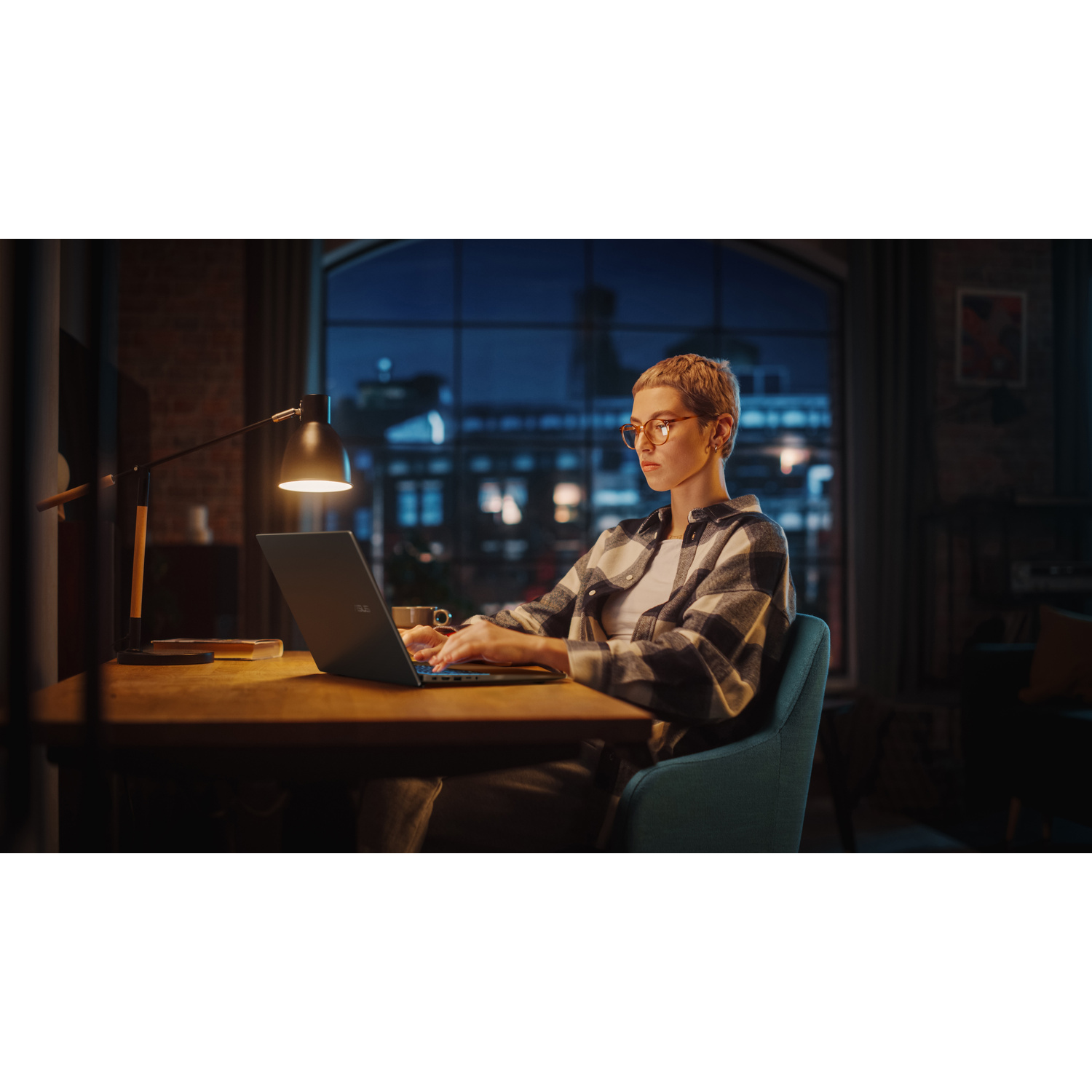 Donna con capelli corti digita su un laptop, illuminata da una lampada da scrivania.