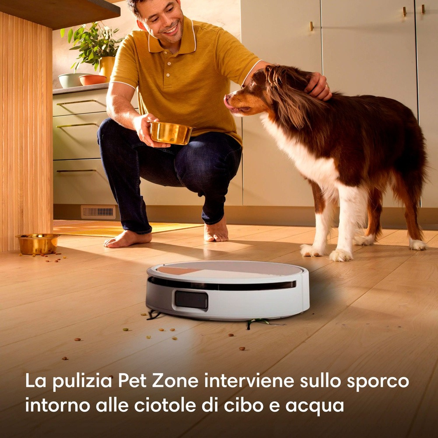 Uomo accarezza cane, robot aspirapolvere pulisce residui cibo.