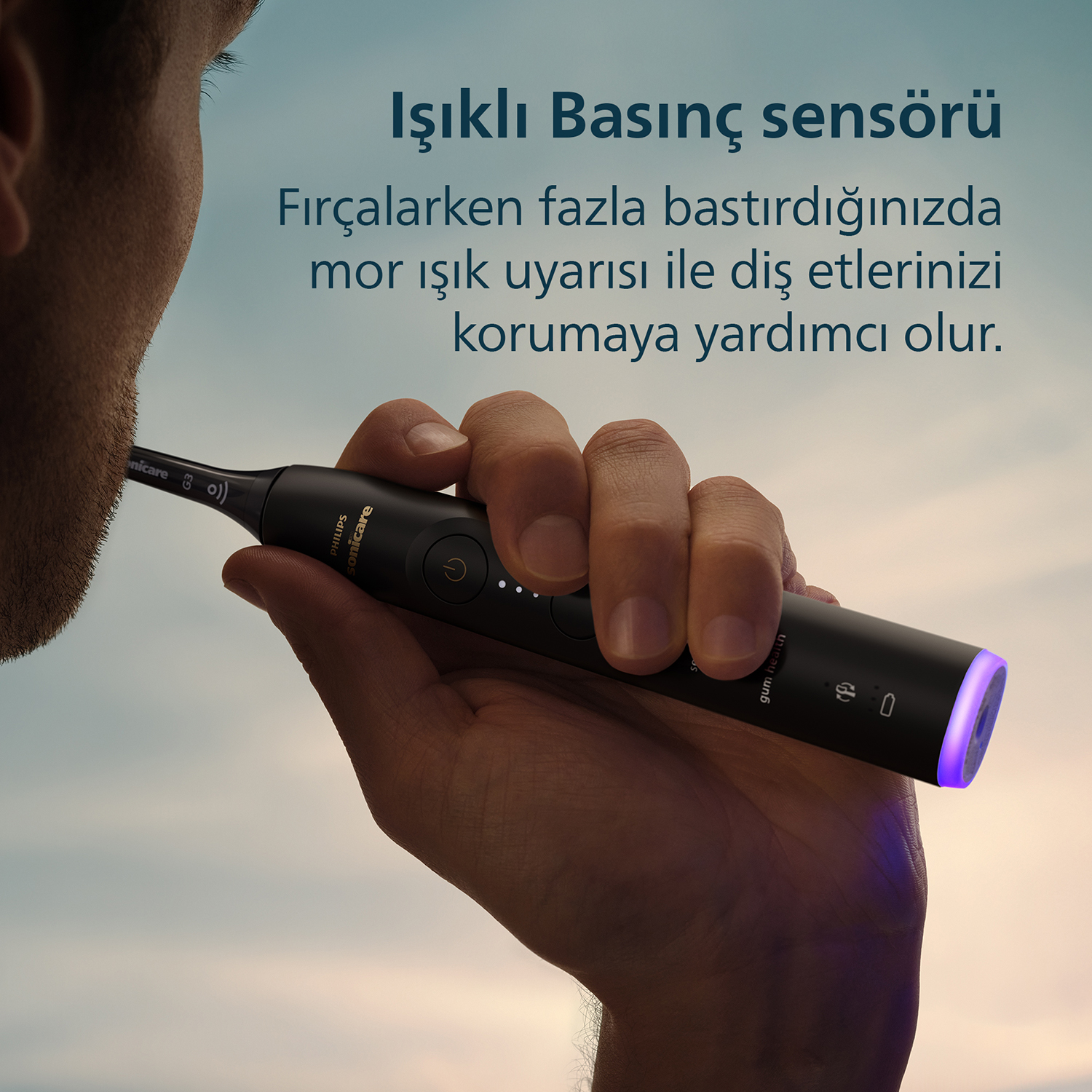 Bir kişi, ucunda mavi ışık bulunan siyah elektrikli diş fırçası tutuyor.