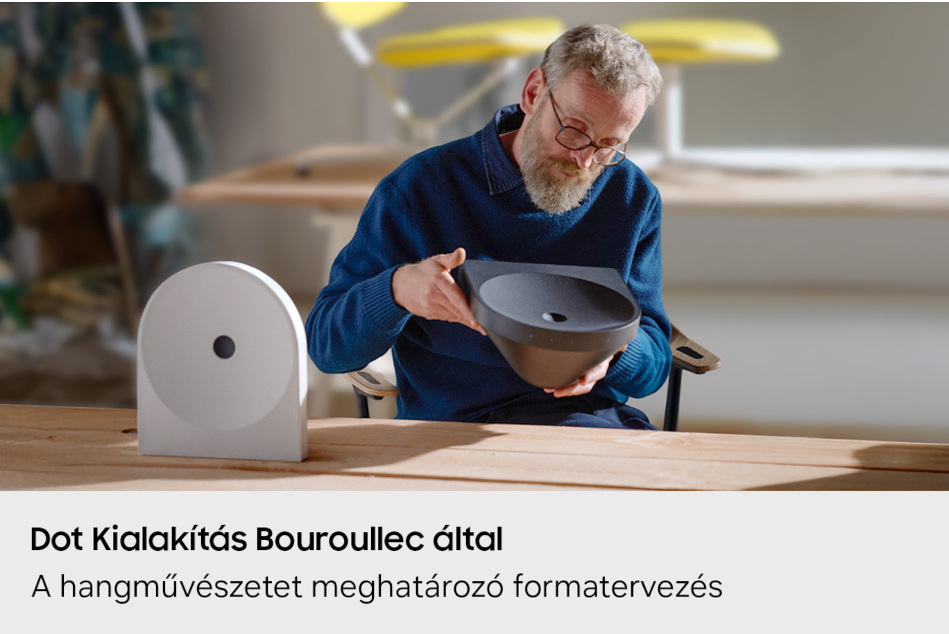 Egy szemüveges férfi egy sötét tálat tart egy műhelyben.