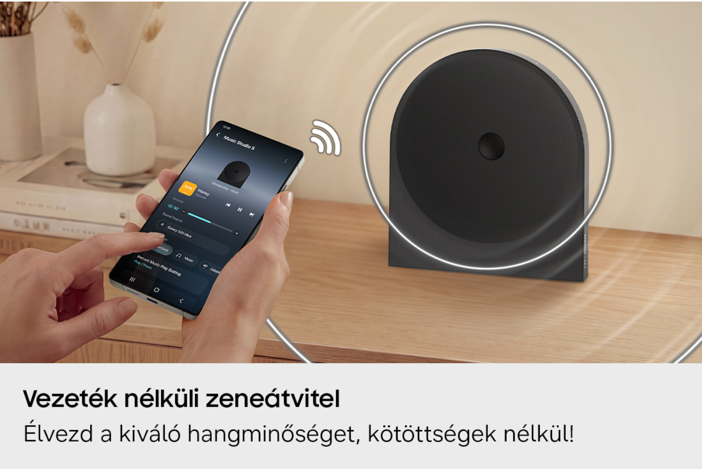 Egy kéz telefonnal zene appal, mellette fekete hangszóró.