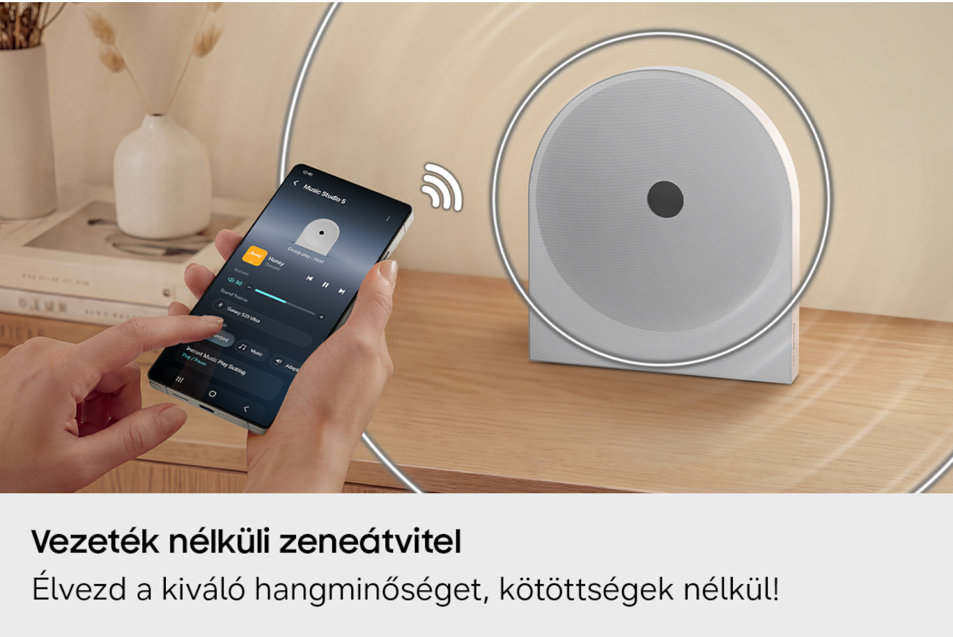 Kézzel tartott telefon zenealkalmazással, mellette fehér hangszóró.