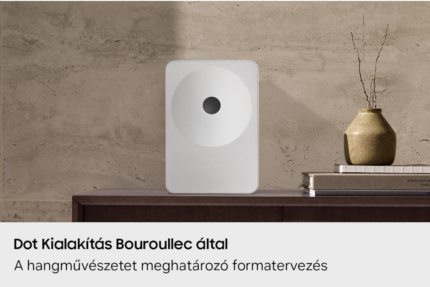Fehér doboz fekete körrel polcon, vázával és könyvekkel.