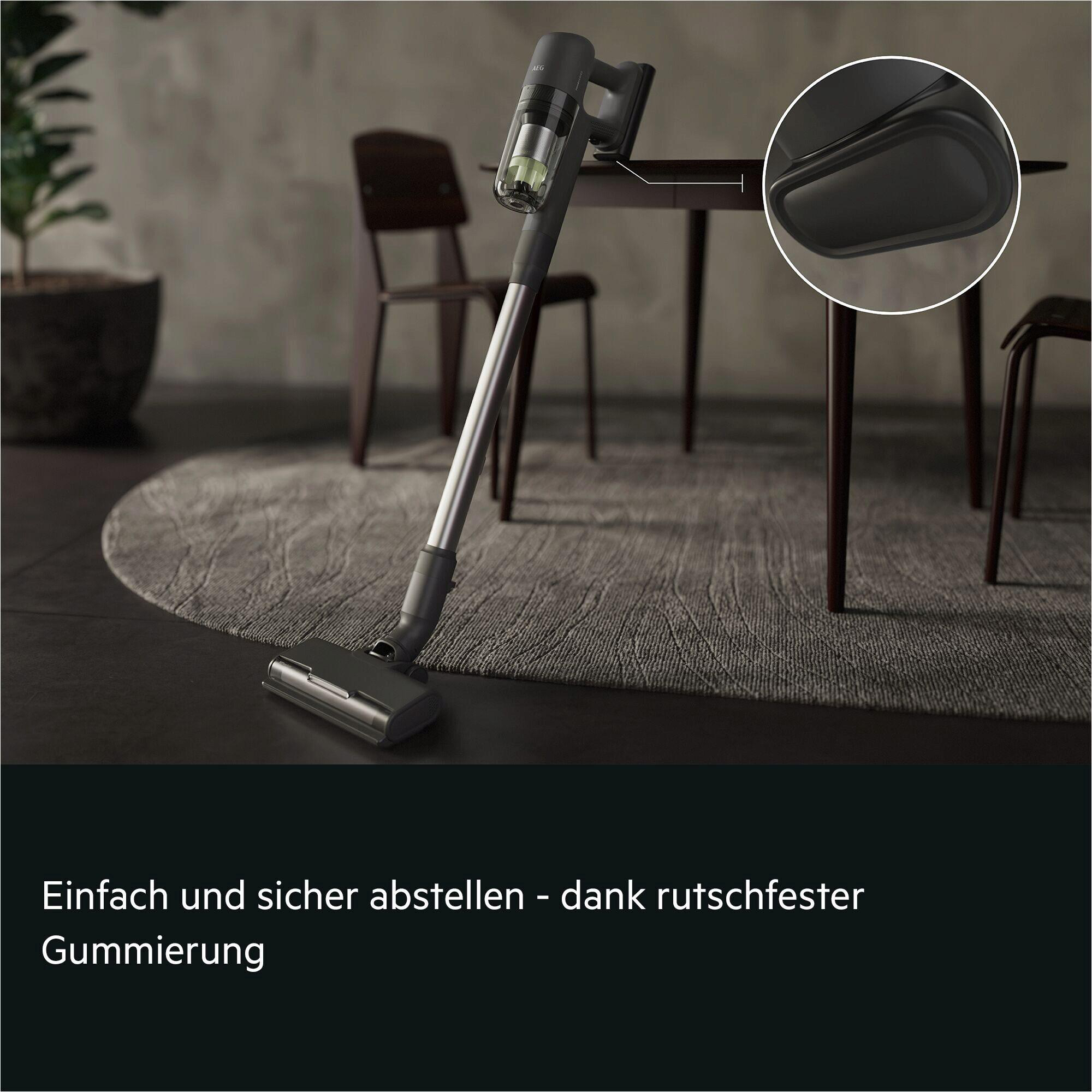 Ein kabelloser Staubsauger steht auf einem Teppich neben einem Tisch und Stühlen.