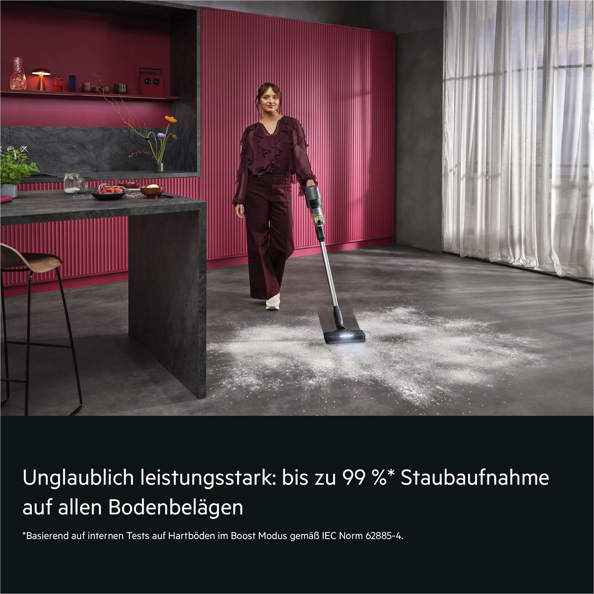 Eine Frau benutzt einen Akku-Staubsauger, um Staub auf einem dunklen Boden aufzusaugen.