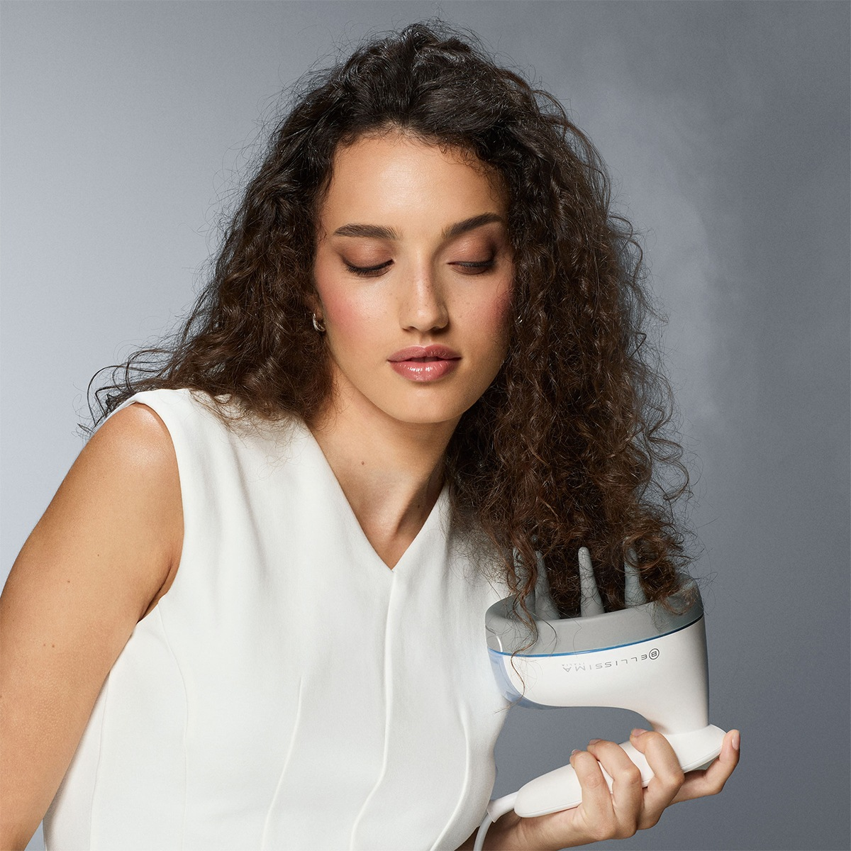 Una mujer con cabello rizado se seca el pelo con un difusor.