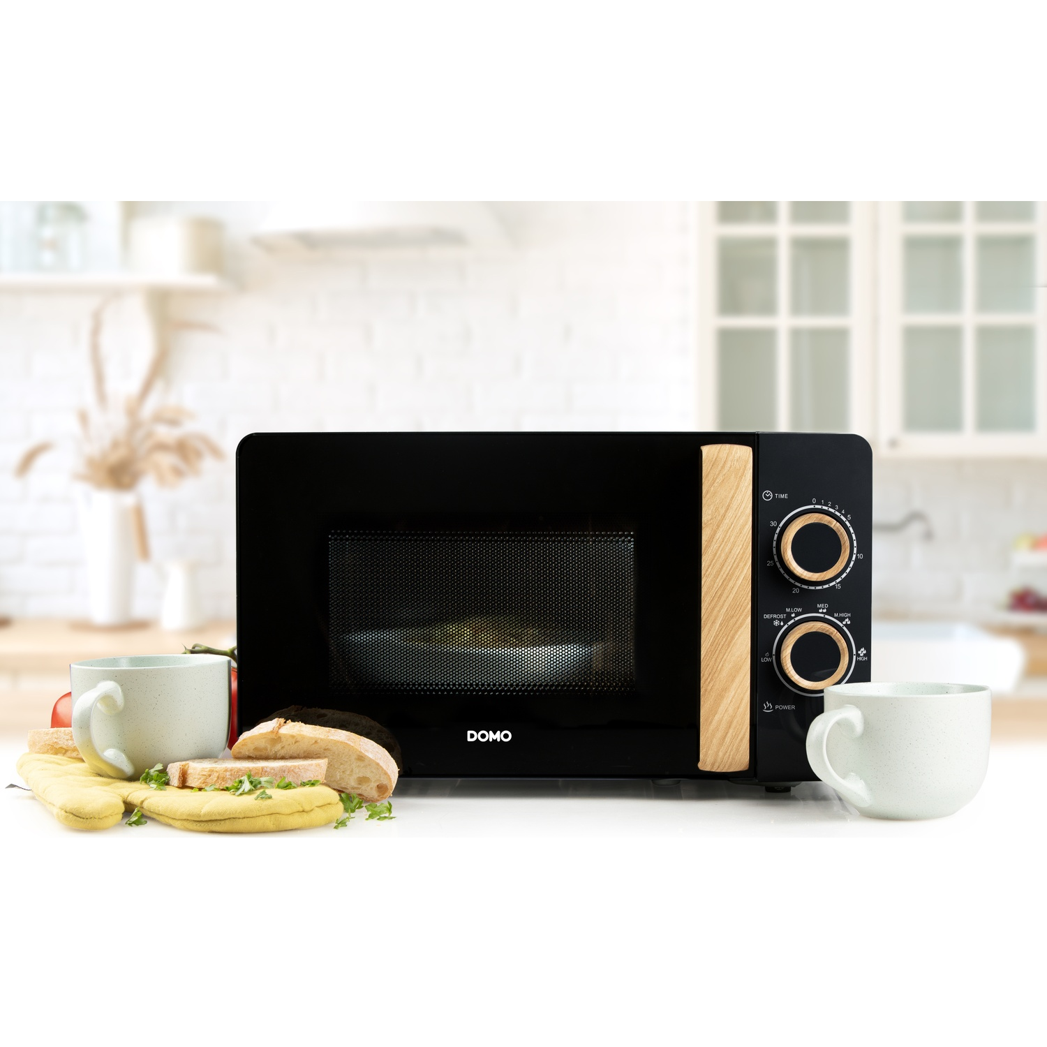 Micro-ondes noir avec accents en bois, pain, tasses et maniques à proximité.