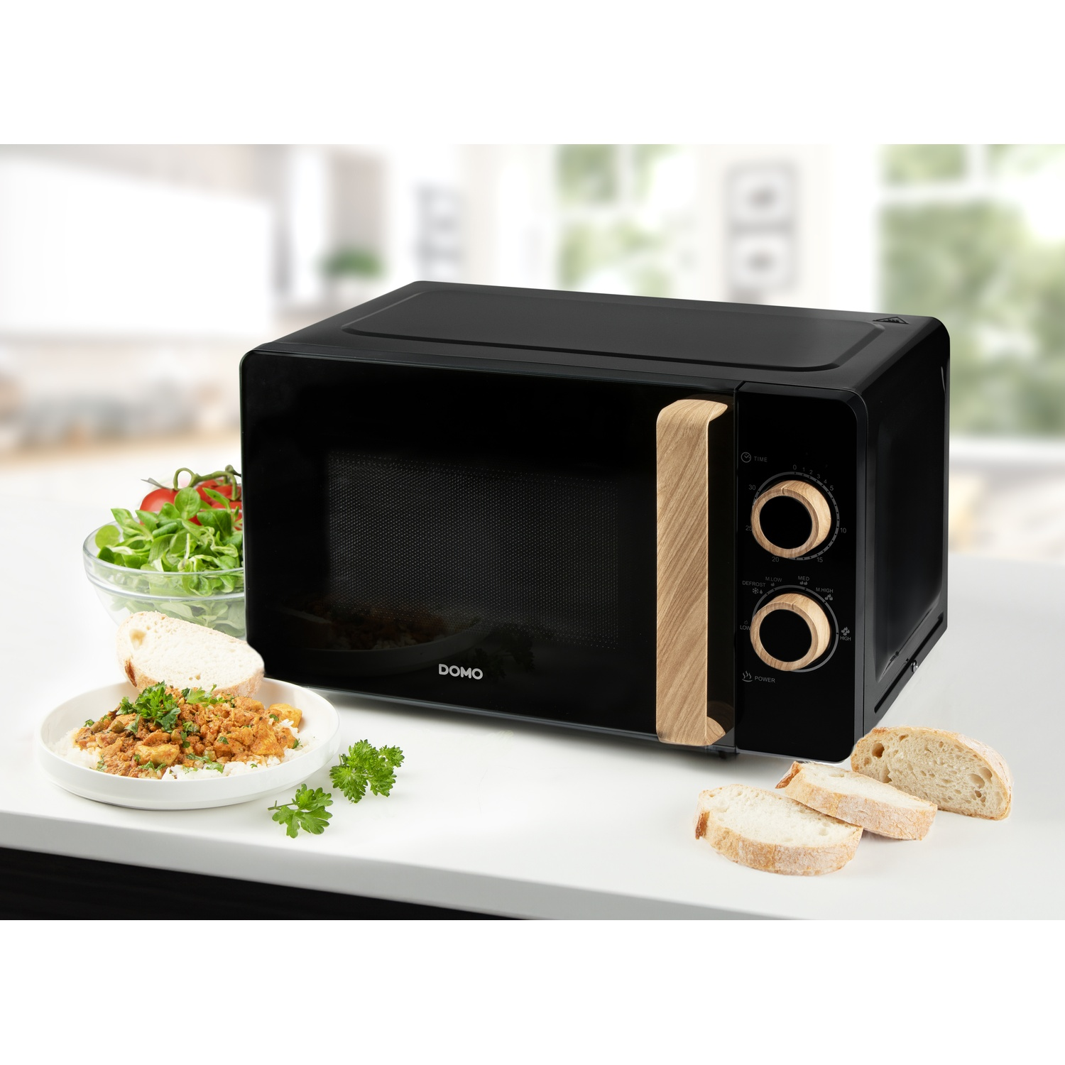 Micro-ondes noir avec accents bois, à côté d'une salade, plat de riz et pain.