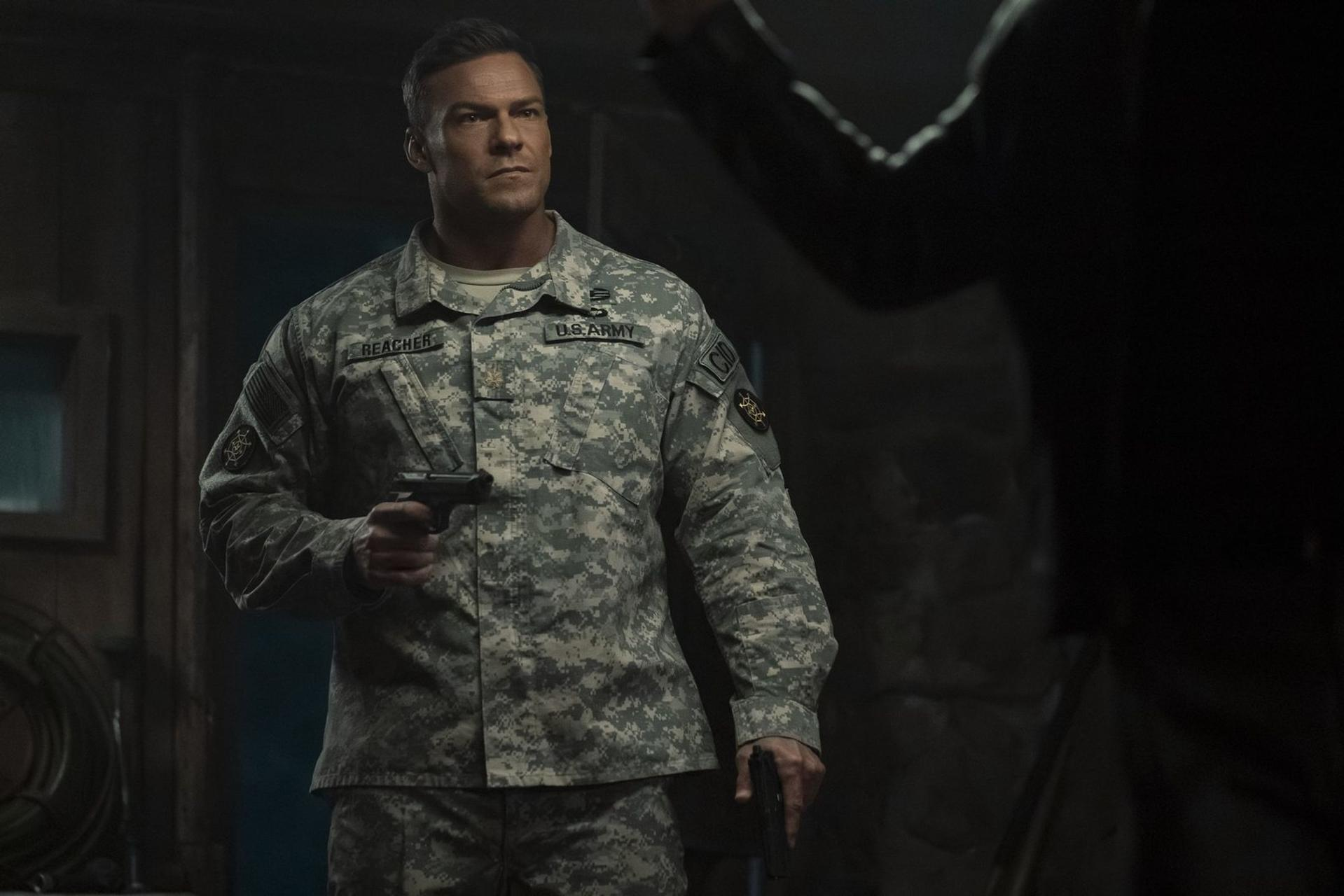 Ein Mann in US-Armeeuniform hält zwei Pistolen in einem dunklen Raum.